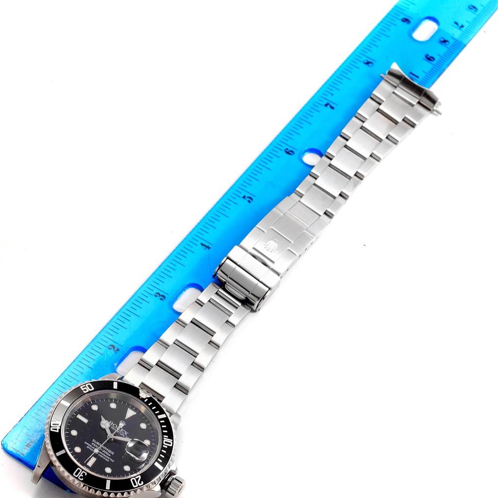 The image shows a Rolex Submariner 16610 Men's Stainless Steel Black Dial 16610 Men's Stainless Steel Black Dial watch lying flat with its band laid out next to a blue ruler.