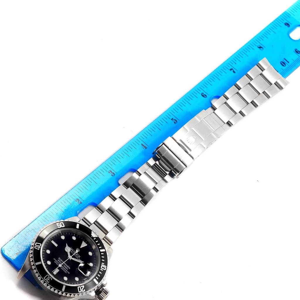 The image shows a Rolex Submariner 16610 Men's Stainless Steel Black Dial 16610 Men's Stainless Steel Black Dial watch fully extended next to a ruler, highlighting the face and bracelet.