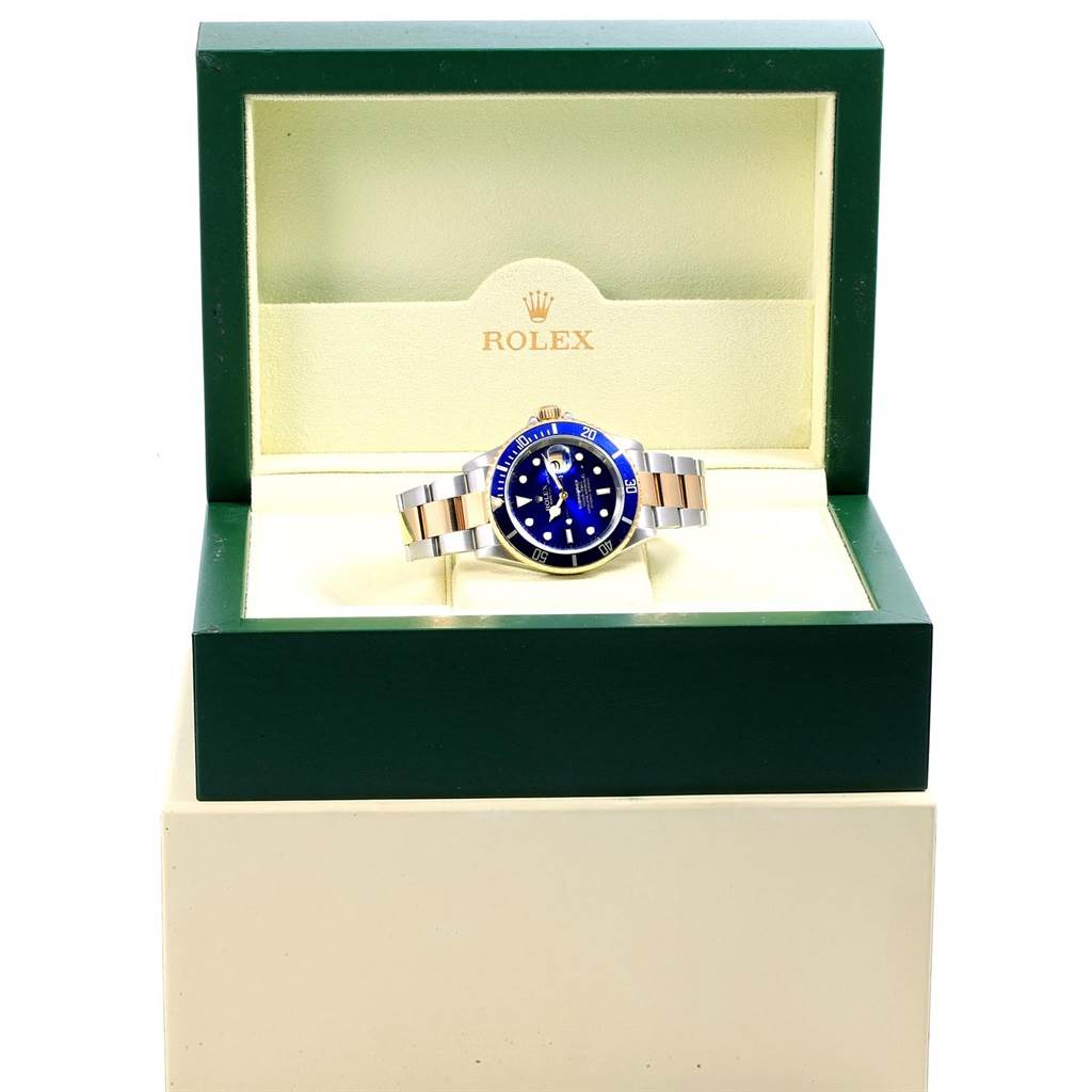 The Rolex Submariner 16613 Men's Steel and Gold (two tone) Blue Dial 16613 Men's Steel and Gold (two tone) Blue Dial watch is shown from the front, inside an open green and cream Rolex box.