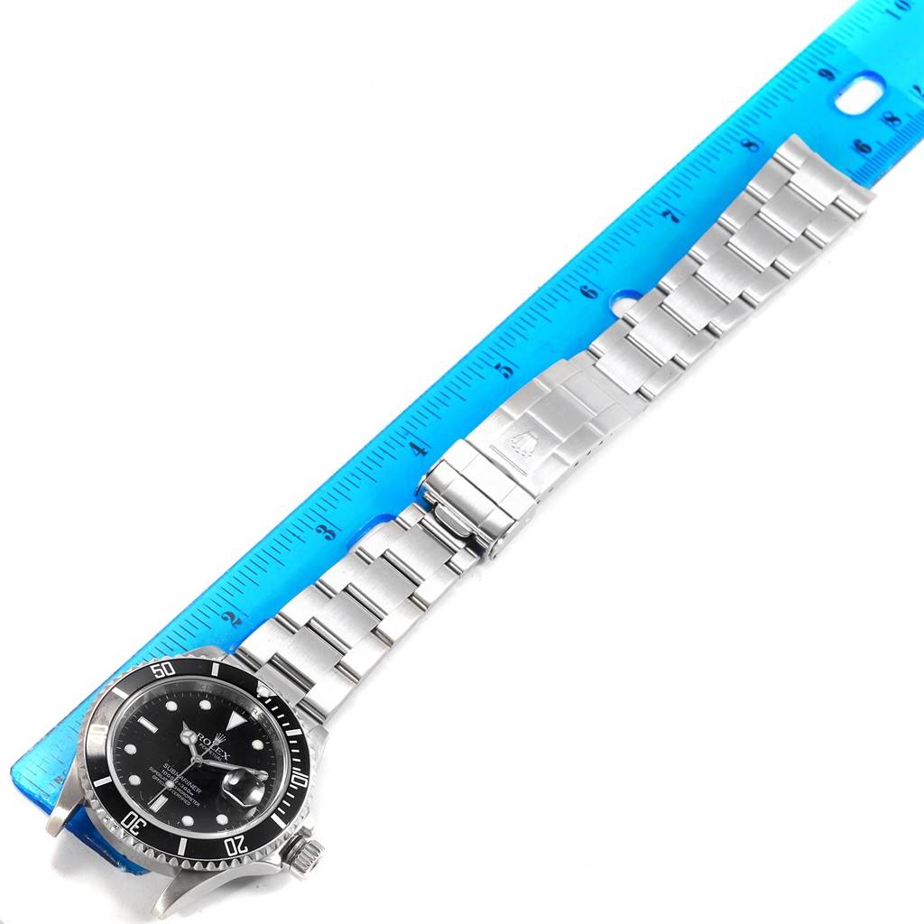 The watch, a Rolex Submariner 16610 Men's Stainless Steel Black Dial 16610 Men's Stainless Steel Black Dial, is shown from a top-down angle alongside a ruler, displaying its bracelet and clasp.