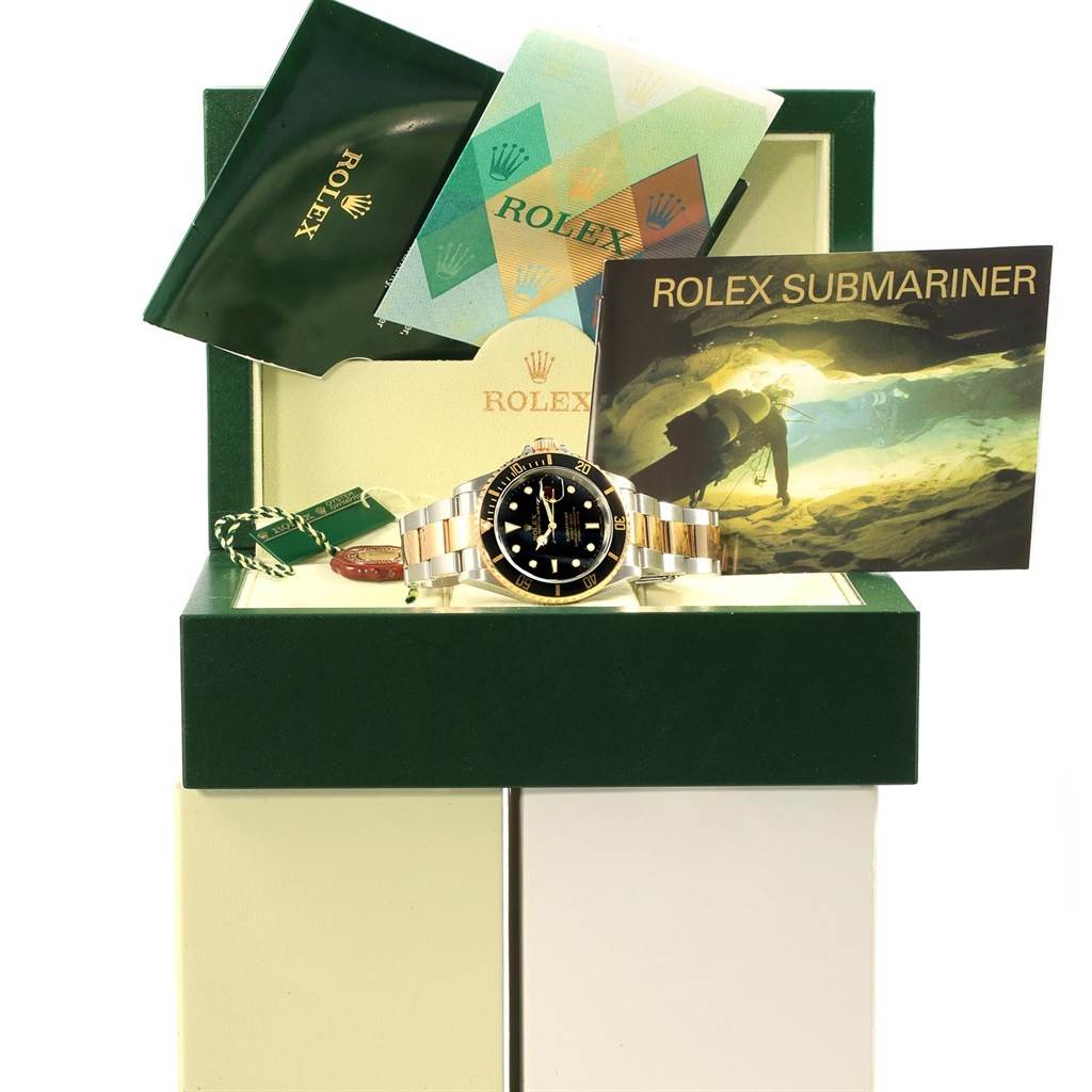The image shows a Rolex Submariner 16613 Men's Steel and Gold (two tone) Black Dial 16613 Men's Steel and Gold (two tone) Black Dial watch along with booklets and tags, all displayed in an open green Rolex box.