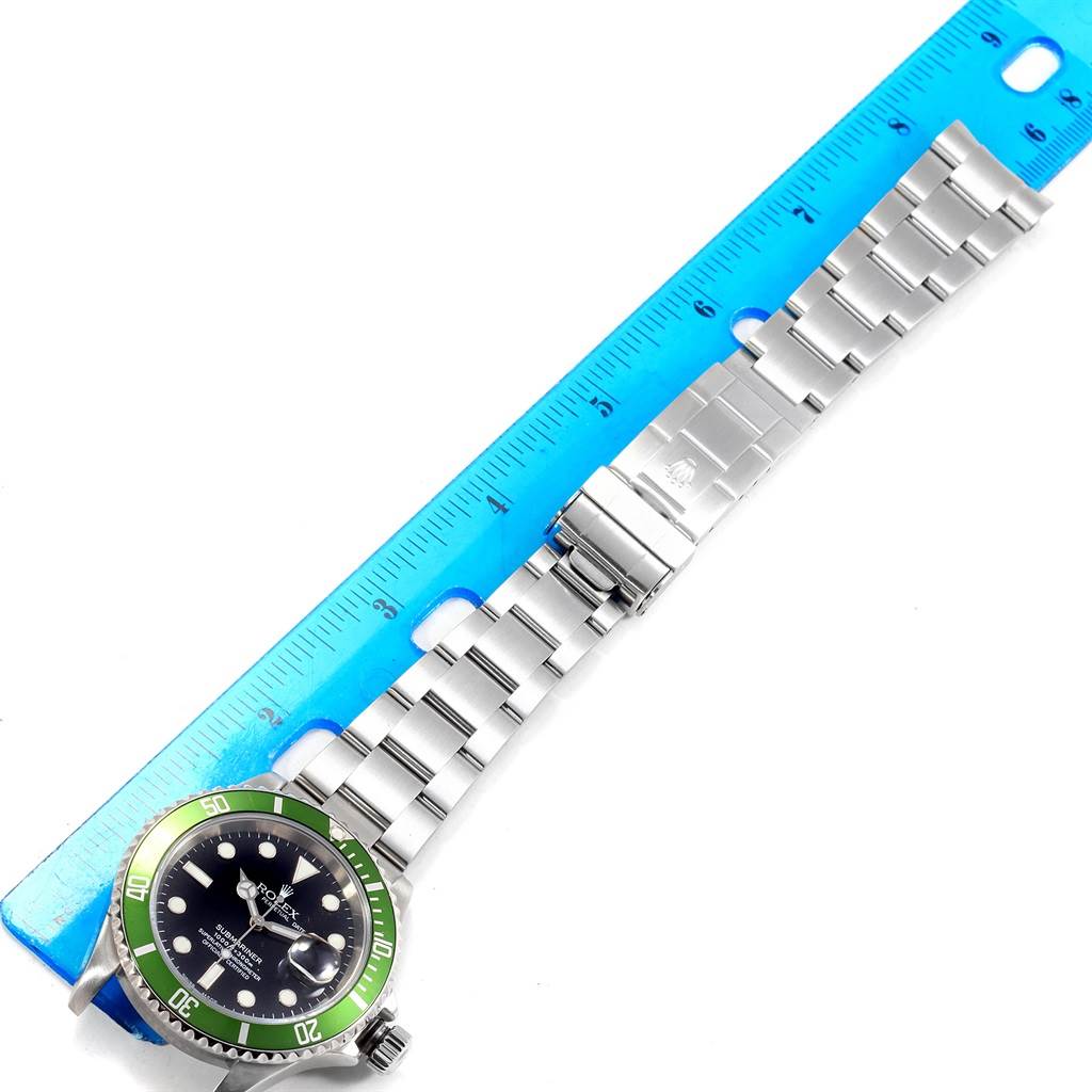 The Rolex Submariner 16610LV Men's Stainless Steel Black Dial 16610LV Men's Stainless Steel Black Dial watch is displayed at an angle, showing the dial, bezel, bracelet, and clasp alongside a blue ruler.