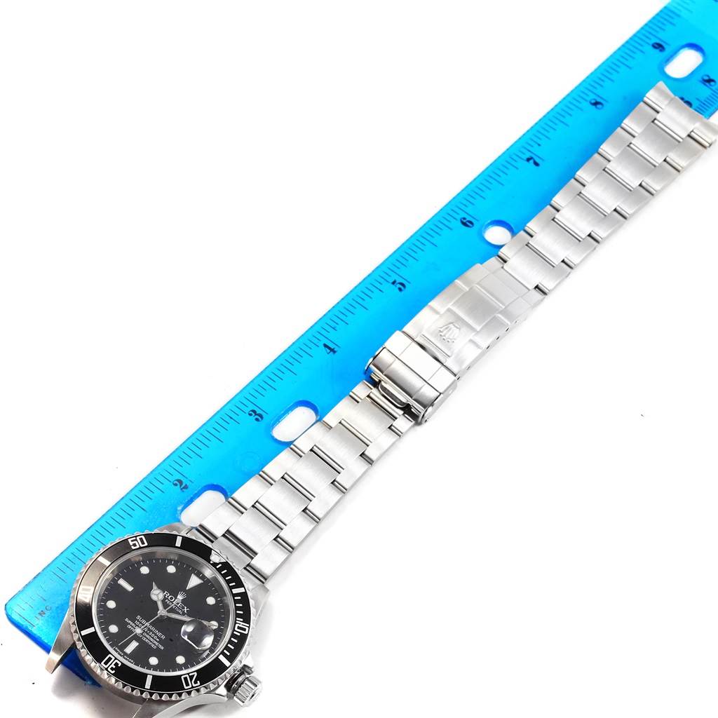 The image shows a Rolex Submariner 16610 Men's Stainless Steel Black Dial 16610 Men's Stainless Steel Black Dial watch laid flat next to a ruler, displaying its face and metal bracelet.