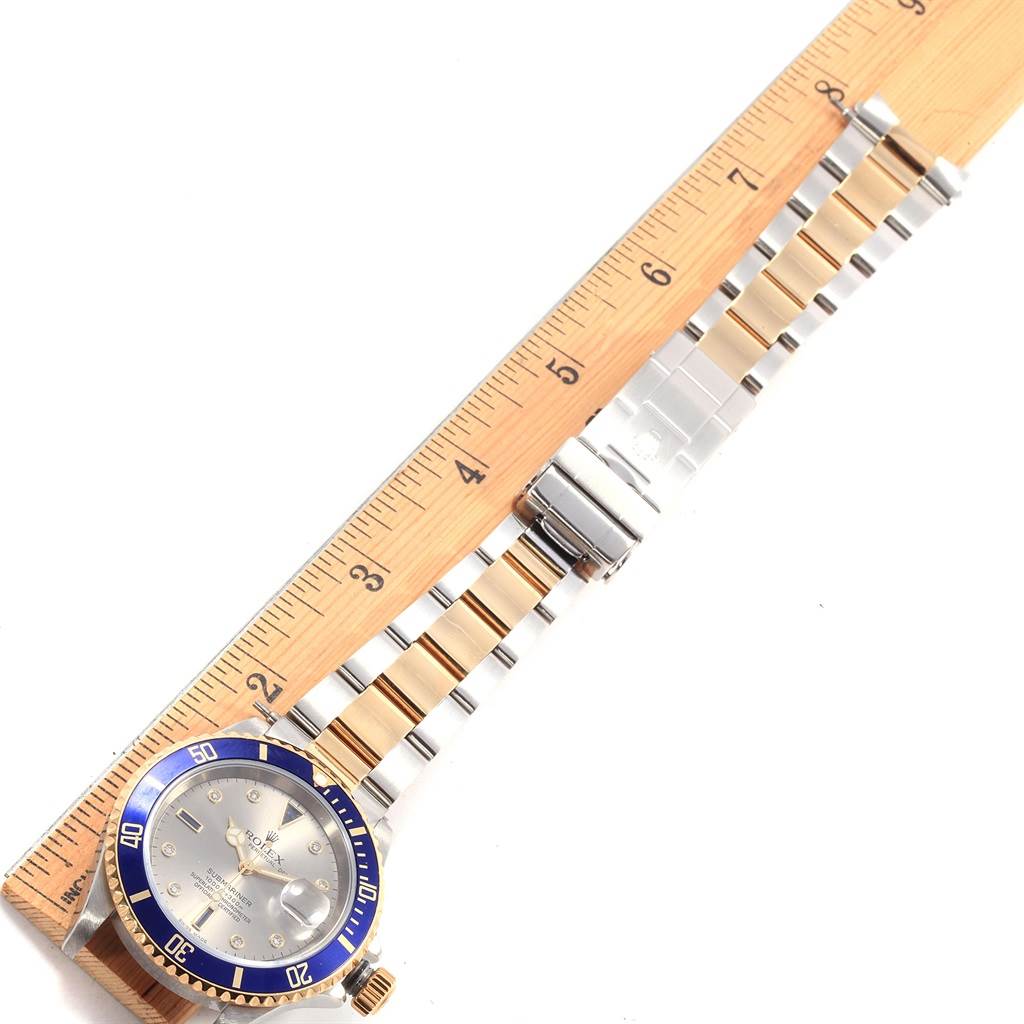 This image shows a Rolex Submariner 16613 Men's Steel and Gold (two tone) Grey Dial 16613 Men's Steel and Gold (two tone) Grey Dial watch laid flat with a ruler beside it, displaying the face, bezel, and metal bracelet.