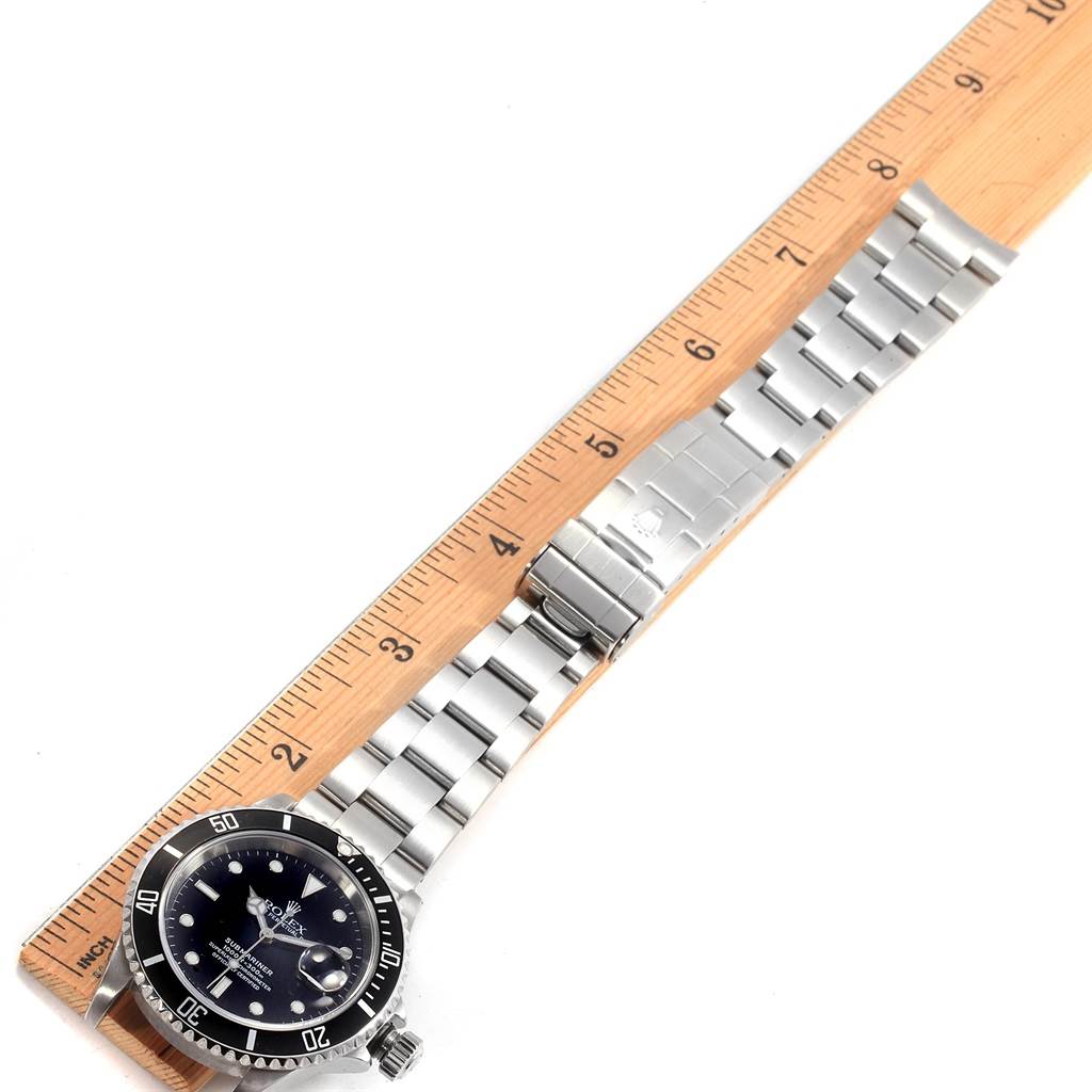 The image shows a top view of a Rolex Submariner 16610 Men's Stainless Steel Black Dial 16610 Men's Stainless Steel Black Dial watch with its face and metal strap placed next to a ruler.