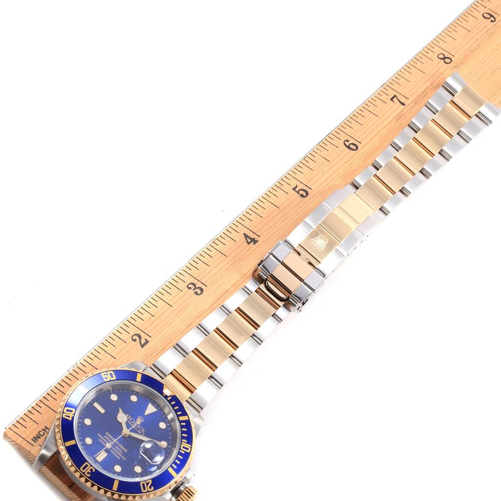The image shows a Rolex Submariner 16613 Men's Steel and Gold (two tone) Blue Dial 16613 Men's Steel and Gold (two tone) Blue Dial watch with a blue dial and bezel, laid flat with a ruler indicating its length.