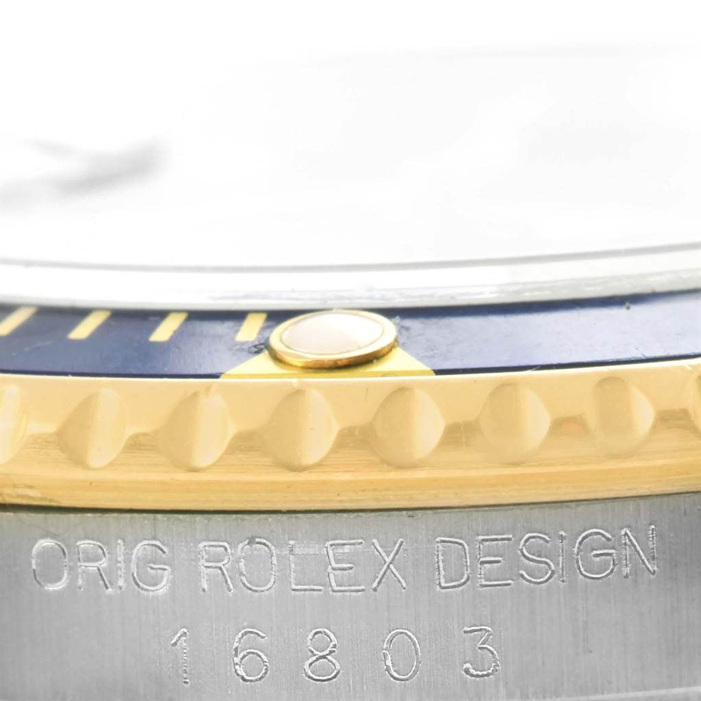 The image shows a close-up of the Rolex Submariner 16803 Men's Steel and Gold (two tone) Blue Dial 16803 Men's Steel and Gold (two tone) Blue Dial model 16803, focusing on the bezel and engraved case details.
