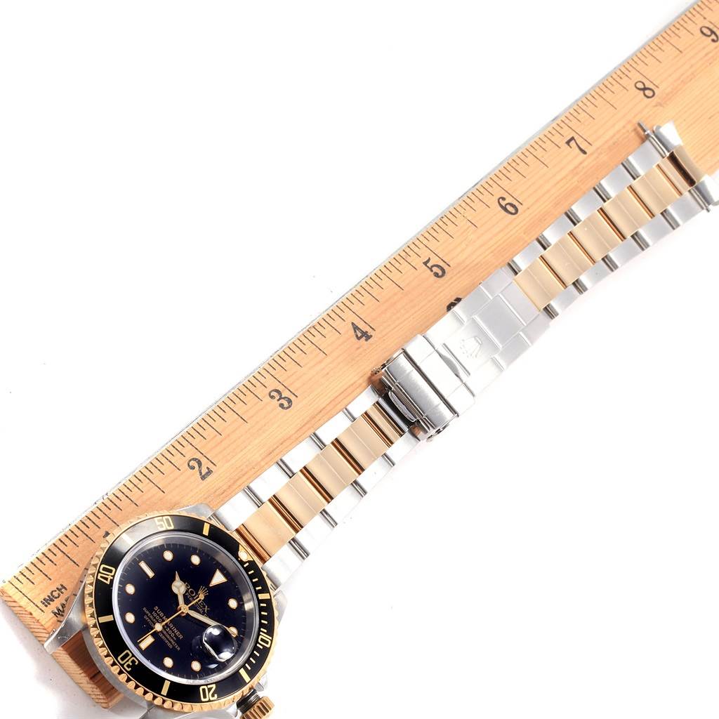 The image shows the face and strap of a Rolex Submariner 16613 Men's Steel and Gold (two tone) Black Dial 16613 Men's Steel and Gold (two tone) Black Dial watch, angled next to a wooden ruler.