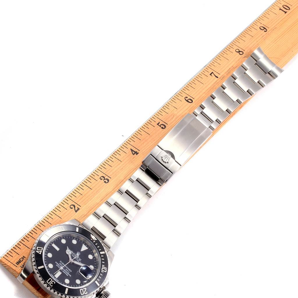 The image shows a side angle of a Rolex Submariner 116610 Men's Stainless Steel Black Dial 116610 Men's Stainless Steel Black Dial watch, highlighting its stainless steel bracelet and clasp, alongside a measurement ruler.