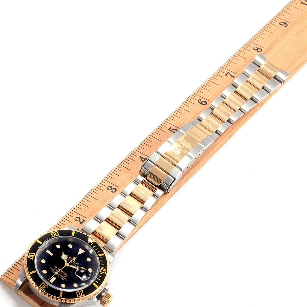 The image shows a top-down view of a Rolex Submariner 16613 Men's Steel and Gold (two tone) Black Dial 16613 Men's Steel and Gold (two tone) Black Dial watch, featuring the watch face, dial, and bracelet placed against a ruler.