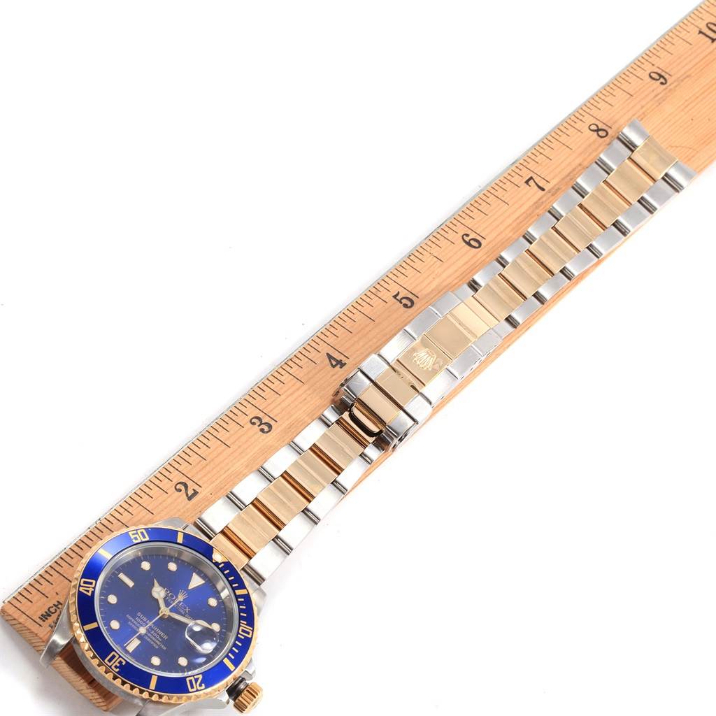 This image shows a Rolex Submariner 16613 Men's Steel and Gold (two tone) Blue Dial 16613 Men's Steel and Gold (two tone) Blue Dial watch with a blue dial and bezel, and a two-tone metal bracelet laid flat next to a ruler.