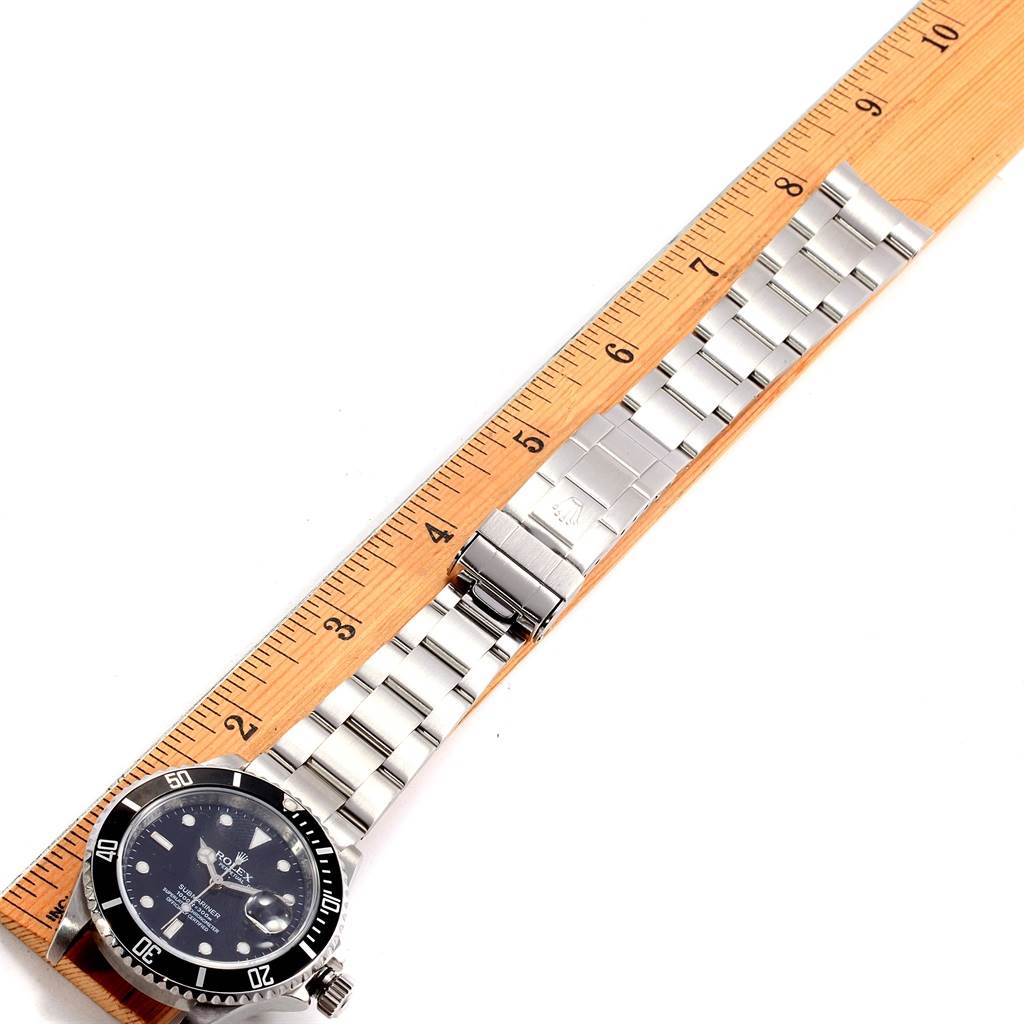 The Rolex Submariner 16610 Men's Stainless Steel Black Dial 16610 Men's Stainless Steel Black Dial watch is displayed face-up, showing the full watch and the metal bracelet next to a ruler for scale.