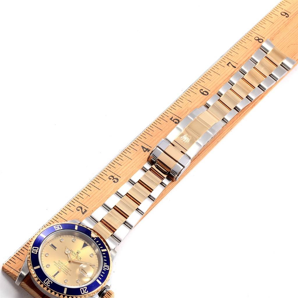 This image shows a Rolex Submariner 16613 Men's Steel and Gold (two tone) Champagne Dial 16613 Men's Steel and Gold (two tone) Champagne Dial watch laid flat on a ruler, highlighting its band, bezel, and face from a top-down angle.
