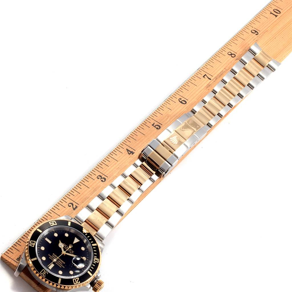 The image shows a Rolex Submariner 16613 Men's Steel and Gold (two tone) Black Dial 16613 Men's Steel and Gold (two tone) Black Dial watch placed alongside a ruler, displaying the face, bezel, and metal bracelet in a flat lay.