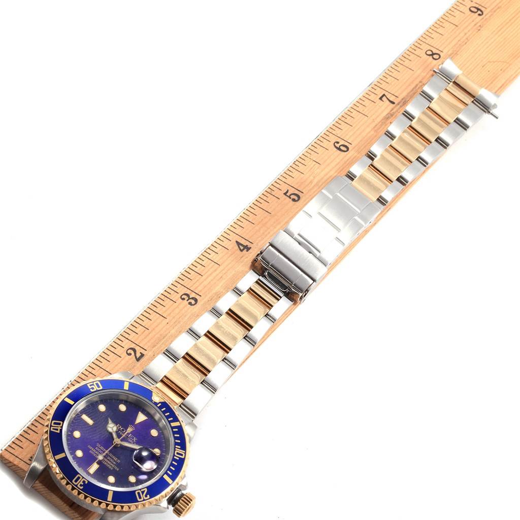 The Rolex Submariner 16613 Men's Steel and Gold (two tone) Blue Dial 16613 Men's Steel and Gold (two tone) Blue Dial watch is viewed from above, showing the face, bezel, and fully extended bracelet against a ruler.