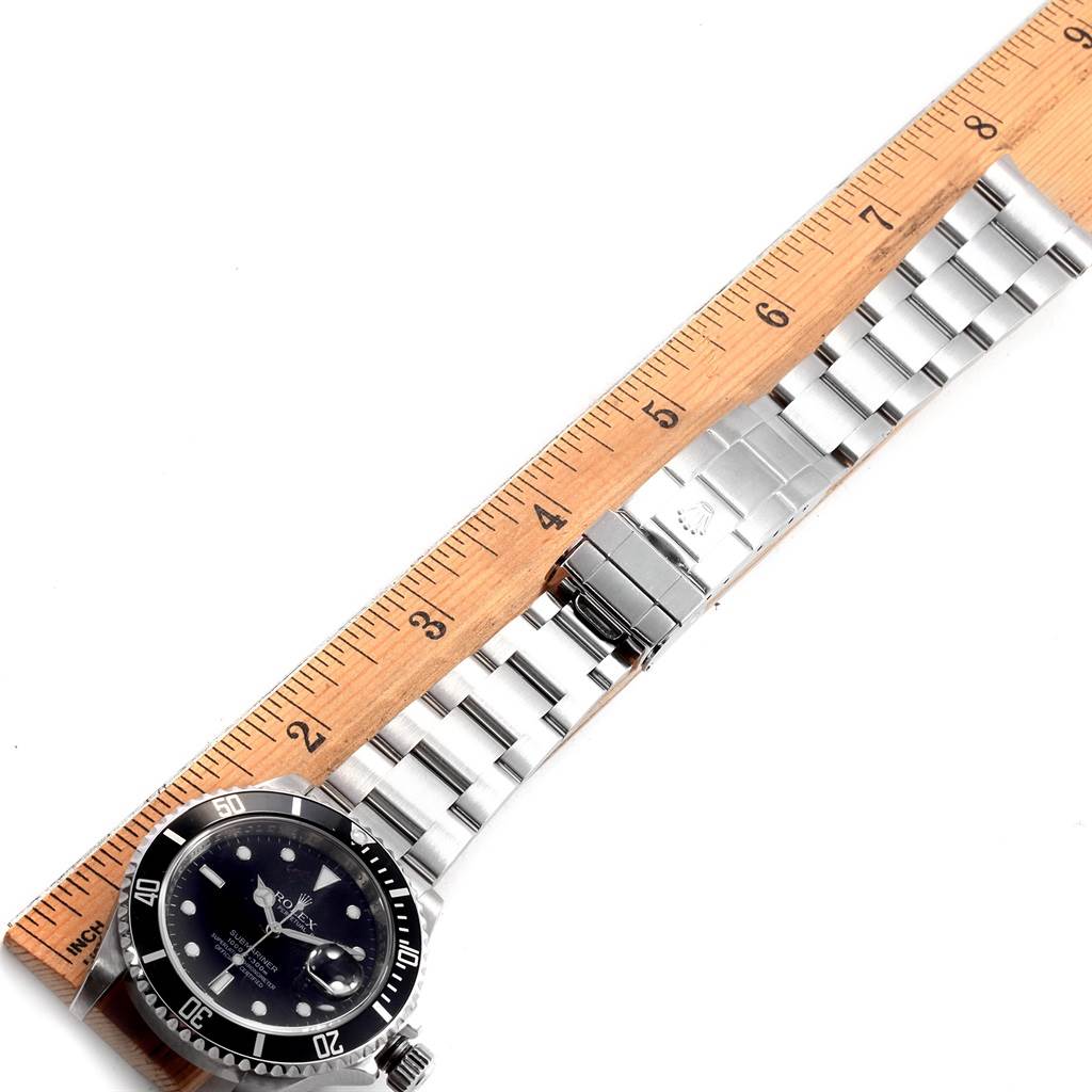 The image shows a side view of a Rolex Submariner 16610 Men's Stainless Steel Black Dial 16610 Men's Stainless Steel Black Dial watch, focusing on the face, bezel, and stainless steel bracelet with a ruler for scale.