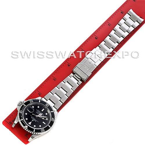 The image shows a Rolex Submariner 16610 Men's Stainless Steel Black Dial 16610 Men's Stainless Steel Black Dial watch laid flat alongside a red measuring ruler.