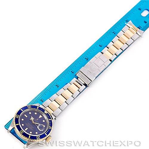 The image shows a Rolex Submariner 16613 Men's Steel and Gold (two tone) Blue Dial 16613 Men's Steel and Gold (two tone) Blue Dial watch from a top view, displaying the face, bezel, and full bracelet next to a ruler for scale.