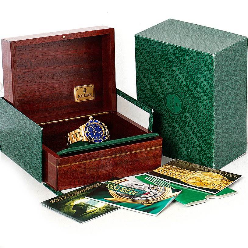 The Rolex Submariner 16618 Men's Yellow Gold Blue Dial 16618 Men's Yellow Gold Blue Dial watch is shown in its open wooden box, with the outer green box and booklets displayed around it.