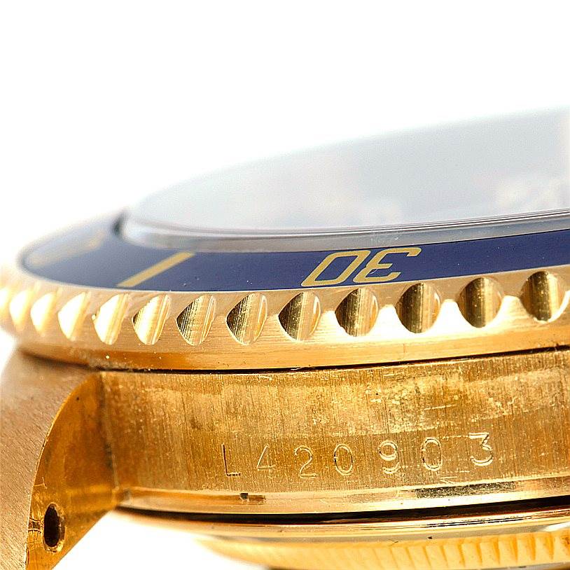 This close-up image of the Rolex Submariner 16618 Men's Yellow Gold Blue Dial 16618 Men's Yellow Gold Blue Dial watch shows the bezel, case, and part of the serial number.