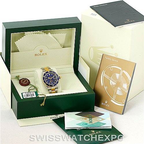 This image shows a Rolex Submariner 16613 Men's Steel and Gold (two tone) Blue Dial 16613 Men's Steel and Gold (two tone) Blue Dial watch at an angle inside its green box along with accessories like booklets, a tag, and a cleaning cloth.