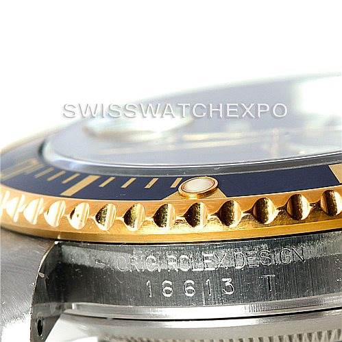 This close-up angle of a Rolex Submariner 16613 Men's Steel and Gold (two tone) Blue Dial 16613 Men's Steel and Gold (two tone) Blue Dial showcases the bezel, part of the crystal, and the "ORIG ROLEX DESIGN" engraving with the serial number.