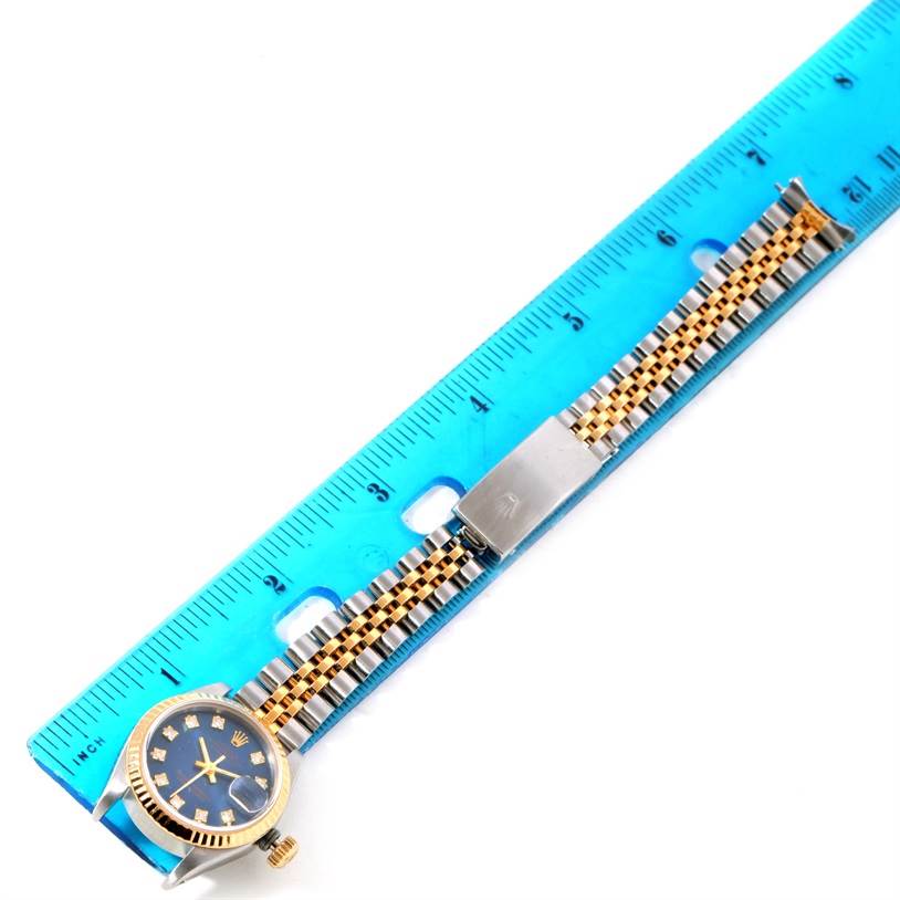 The Rolex Datejust 69173 Women's Stainless Steel Blue Dial 69173 Women's Stainless Steel Blue Dial watch, shown from a top view, features a blue face, bezel, and metal band next to a blue ruler for scale.