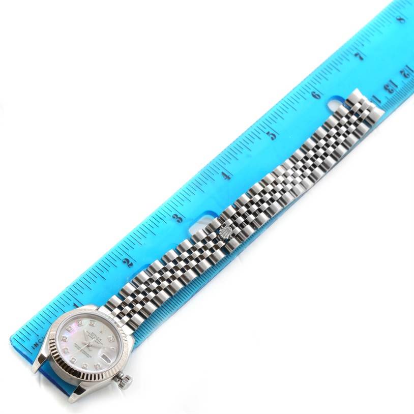 The Rolex Datejust 179174 Women's Stainless Steel Mother of Pearl Dial 179174 Women's Stainless Steel Mother of Pearl Dial watch is shown from a top-down angle with its case, dial, and bracelet visible next to a blue ruler.