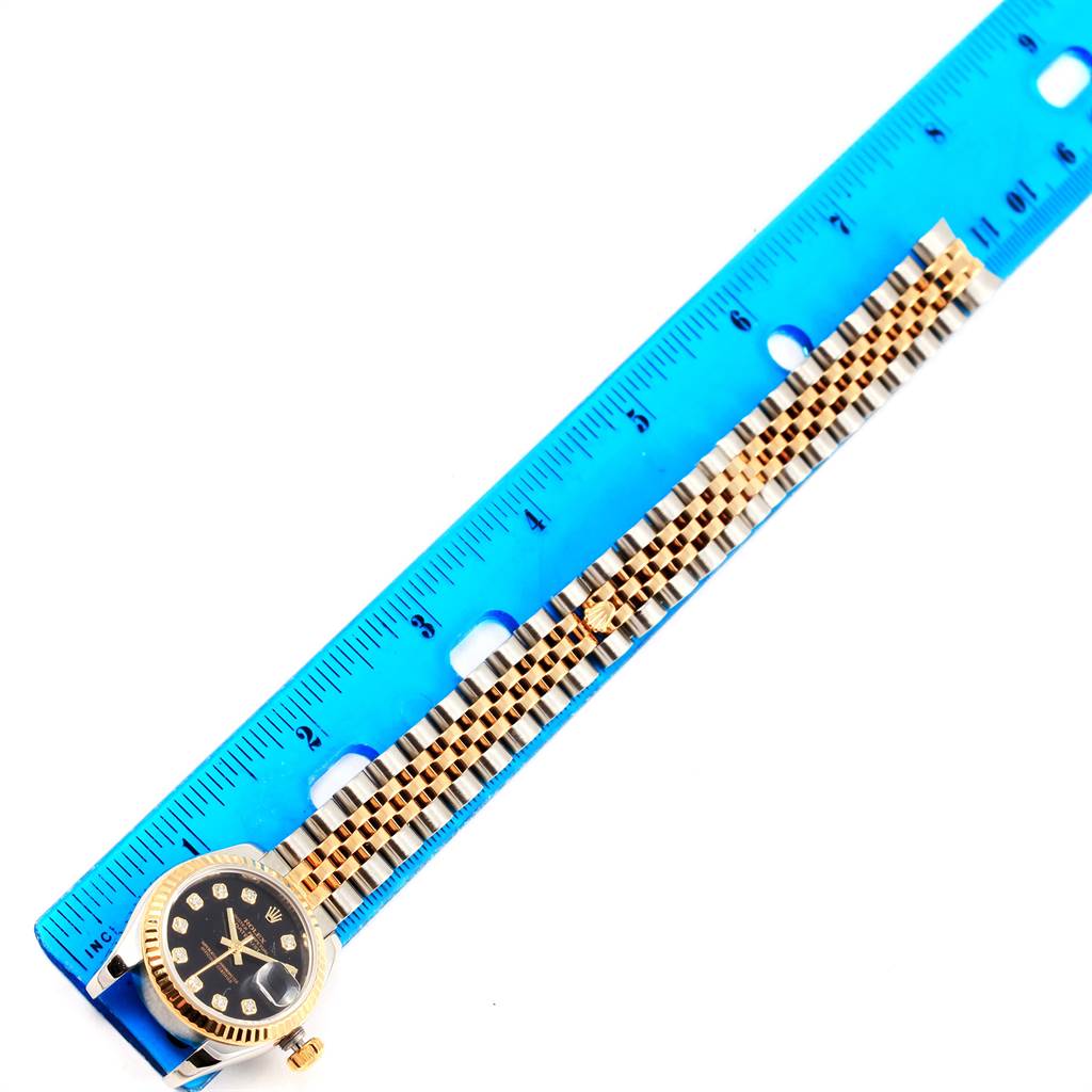 The image shows a gold Rolex Datejust 179173 Women's Steel and Gold (two tone) Black Dial 179173 Women's Steel and Gold (two tone) Black Dial watch laid next to a blue ruler, displaying its bracelet and part of the dial.