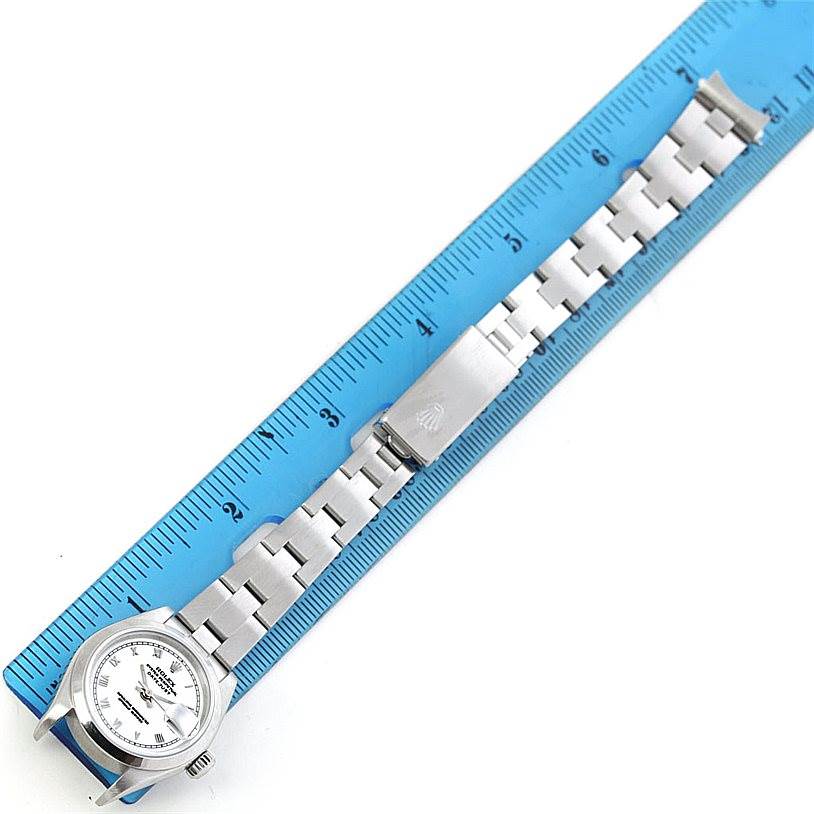 The Rolex Datejust 79160 Women's Stainless Steel White Dial 79160 Women's Stainless Steel White Dial watch is shown from a top-down angle, with its face and metal bracelet, against a blue ruler background.