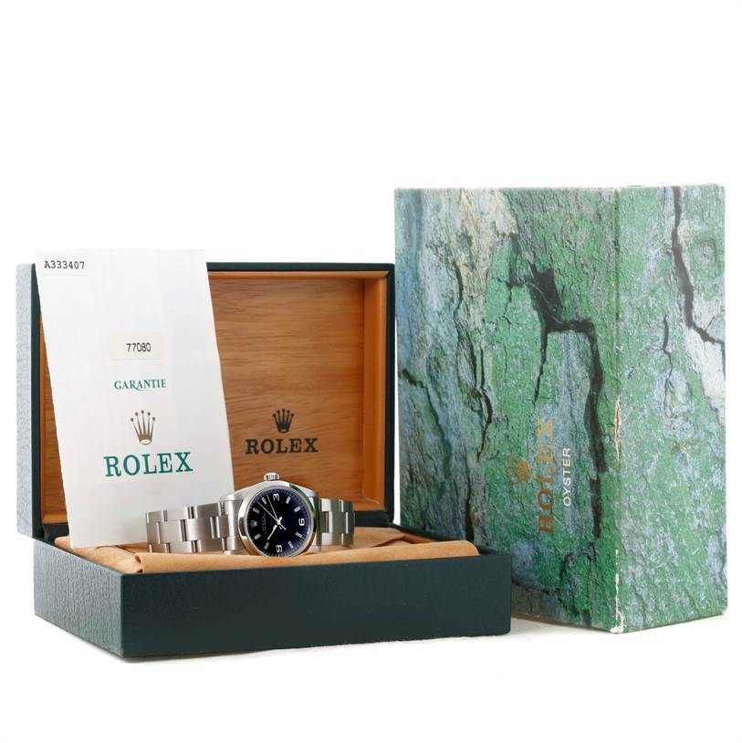 The Rolex Mid-Size 77080 Men's Stainless Steel Black Dial 77080 Men's Stainless Steel Black Dial watch and warranty card are displayed inside an open wooden box with the outer box placed beside it at an angle.