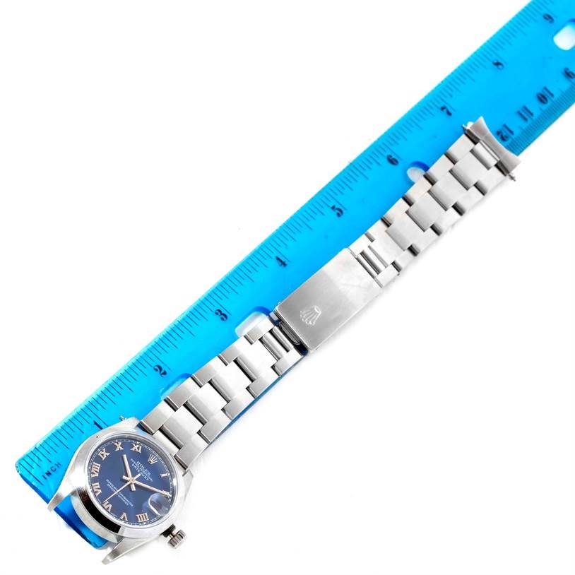 The image shows a Rolex Mid-Size 68240 Women's Stainless Steel Blue Dial 68240 Women's Stainless Steel Blue Dial model watch laid flat against a blue ruler, displaying its silver bracelet and blue dial.
