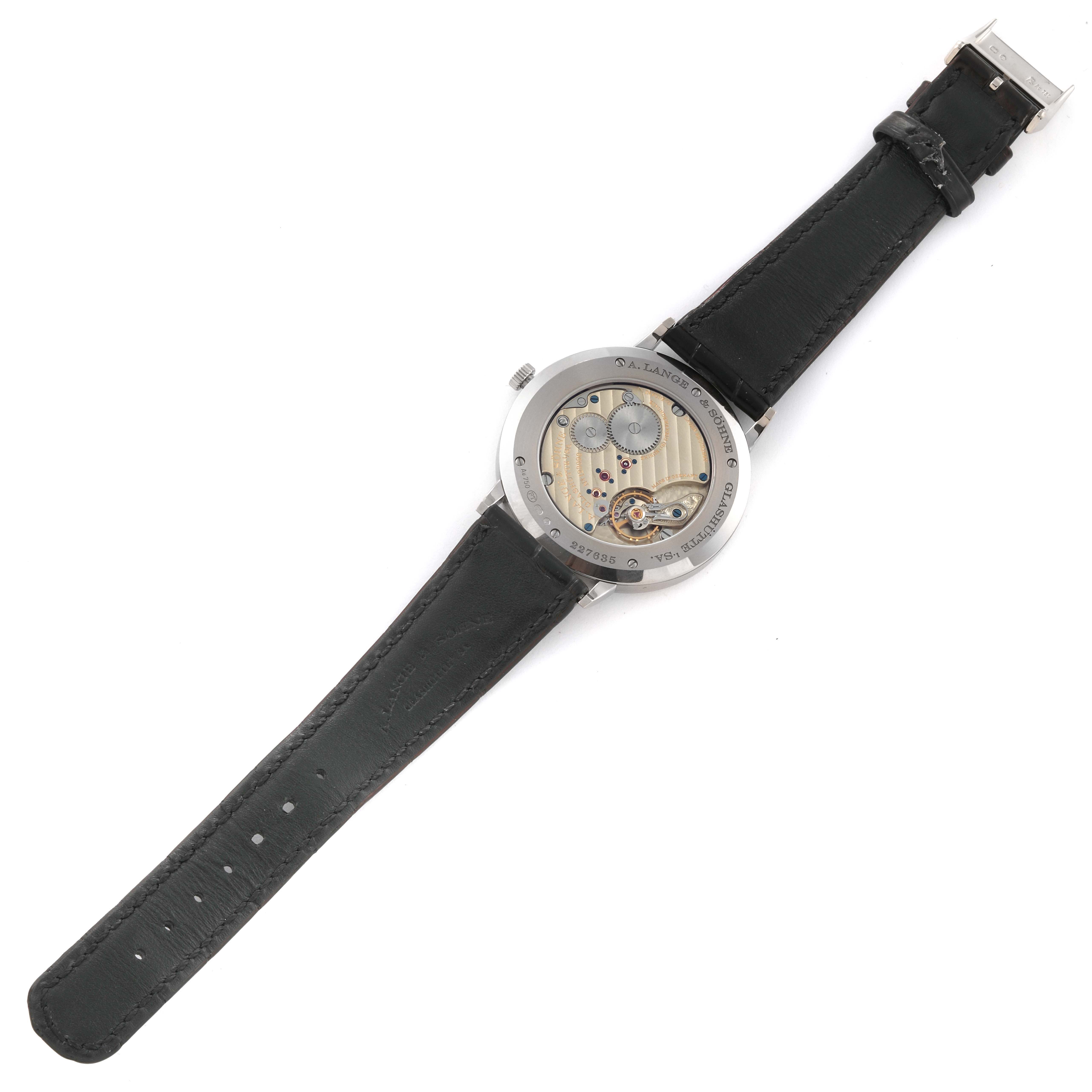 The image shows the back view of an A. Lange & Sohne Saxonia 211.027 Men's White Gold Silver Dial watch, highlighting its movement and black leather strap.