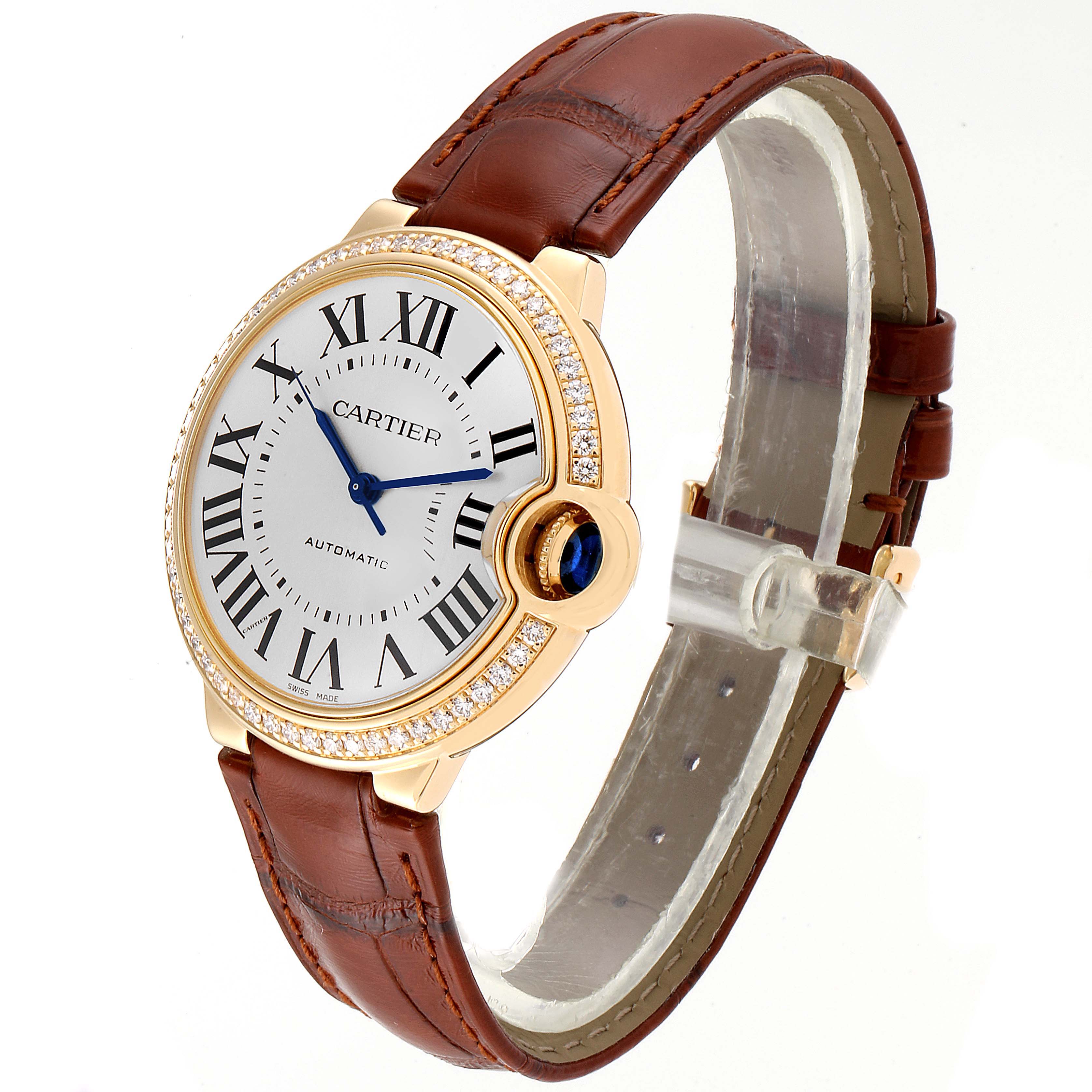 The Cartier Ballon Bleu WE900451 Women's Yellow Gold Silver Dial WE900451 Women's Yellow Gold Silver Dial watch is shown at an angle displaying the face, Roman numerals, blue hands, diamond bezel, brown strap, and crown.