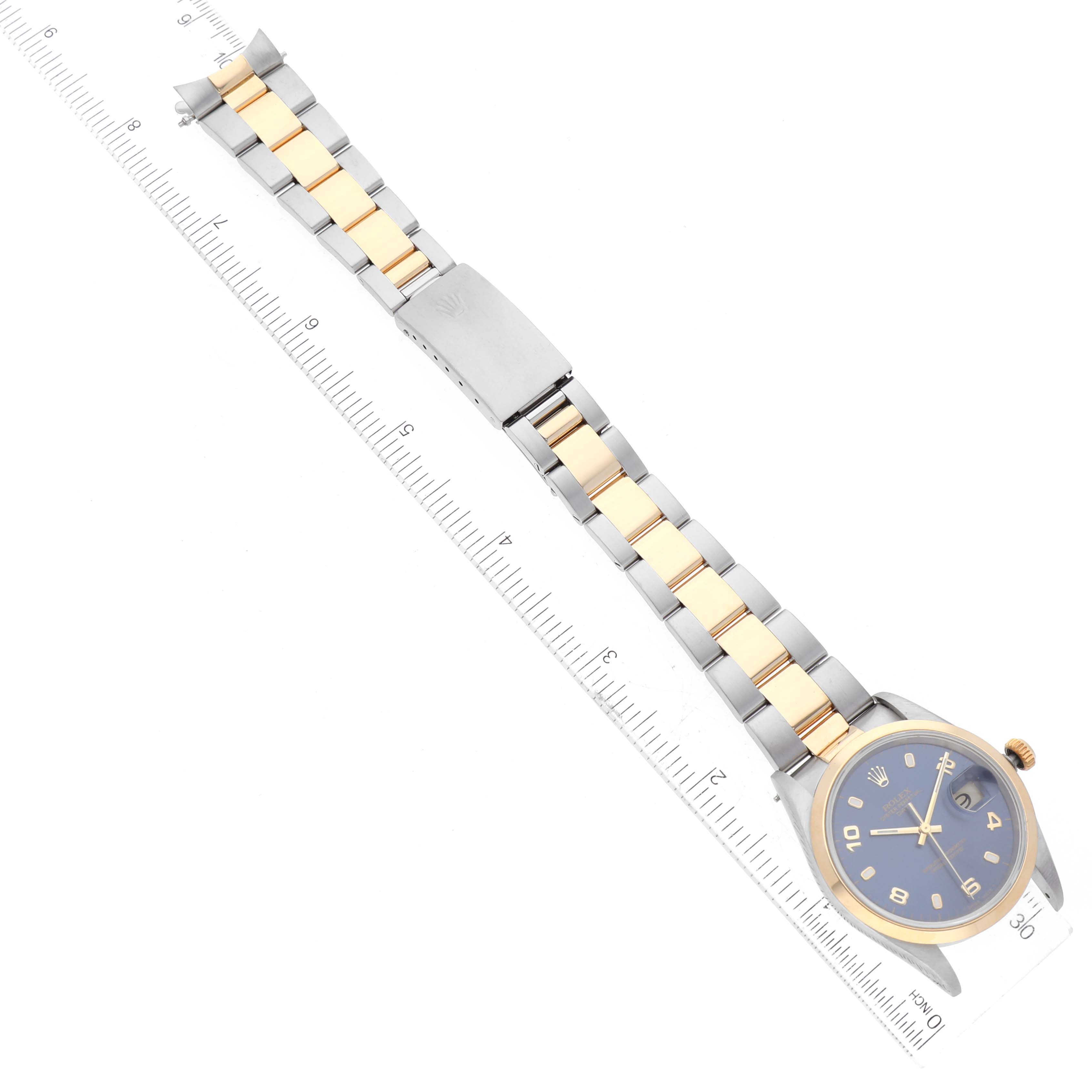 This image shows a Rolex Date 15203 Men's Steel and Gold (two tone) Blue Dial 15203 Men's Steel and Gold (two tone) Blue Dial model watch laid flat with its bracelet extended beside a ruler.