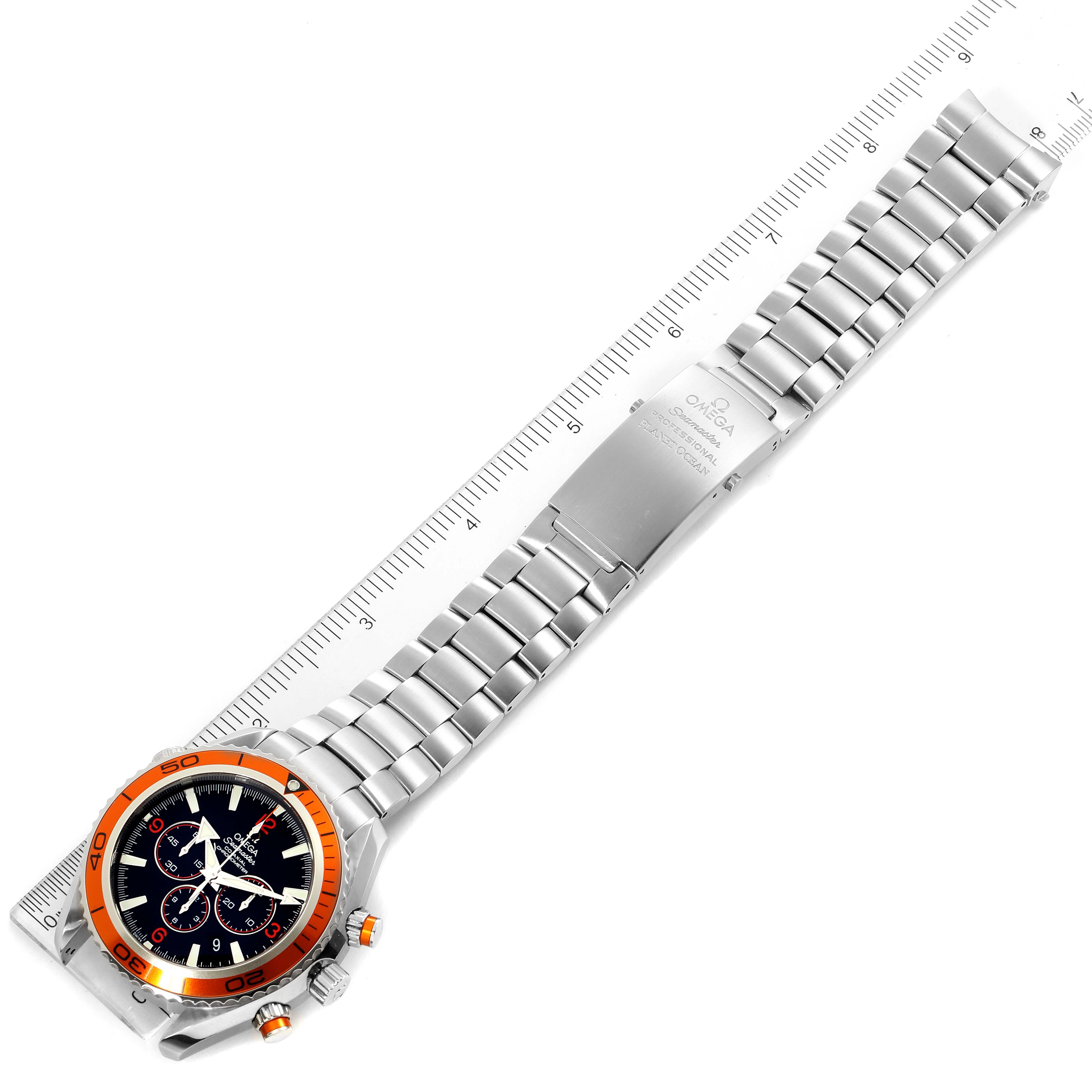 The image shows an overhead view of the Omega Planet Ocean 2218.50.00 Men's Stainless Steel Black Dial 2218.50.00 Men's Stainless Steel Black Dial watch, highlighting its full bracelet and watch face next to a ruler.