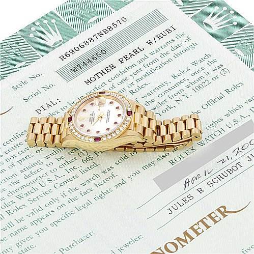 The image shows a Rolex President 69068 Women's Yellow Gold Mother of Pearl Dial 69068 Women's Yellow Gold Mother of Pearl Dial model watch lying flat on its side, displaying its gold bracelet and round face with ruby indices.