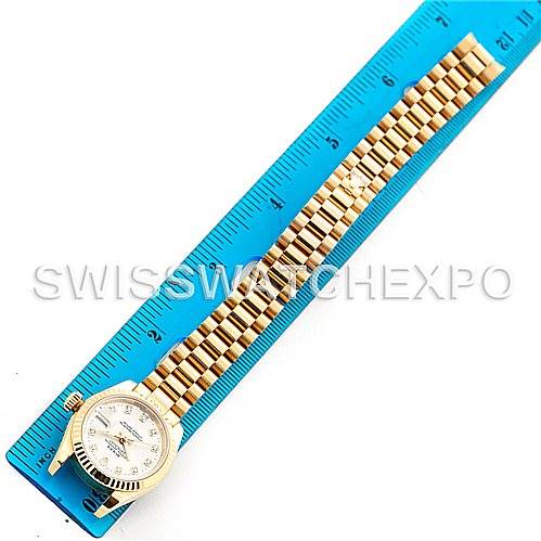 The image shows a top view of a Rolex President 179178 Women's Yellow Gold Silver Dial 179178 Women's Yellow Gold Silver Dial model watch with the band extended next to a blue ruler.