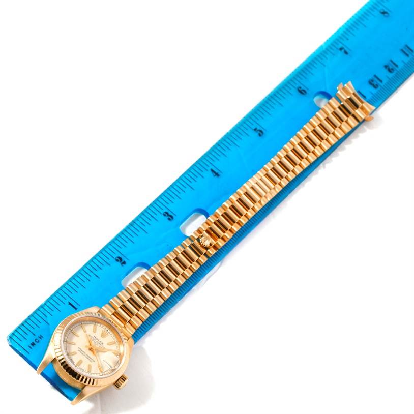 The Rolex President 69178 Women's Yellow Gold Beige Dial 69178 Women's Yellow Gold Beige Dial model watch is shown from an overhead angle, featuring its face and bracelet placed next to a ruler.