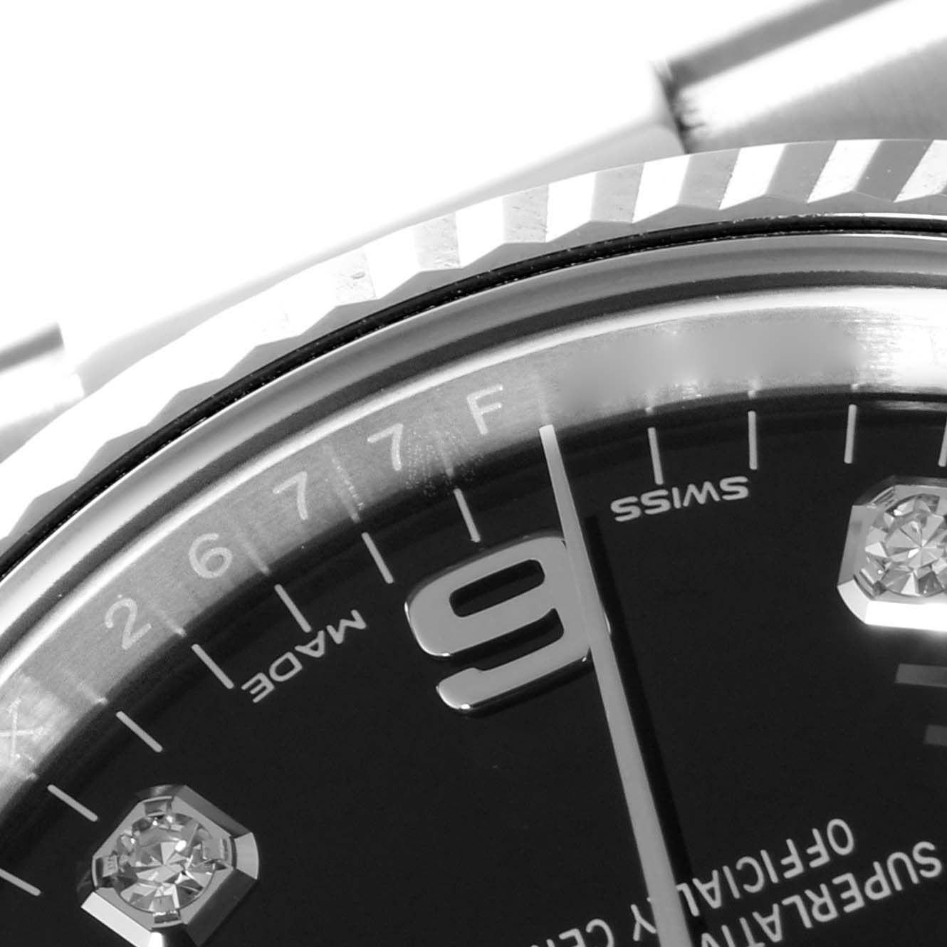 This close-up shot of the Rolex Date 115234 Men's Stainless Steel Black Dial 115234 Men's Stainless Steel Black Dial model watch shows part of the bezel, the number 9, and diamond hour markers.