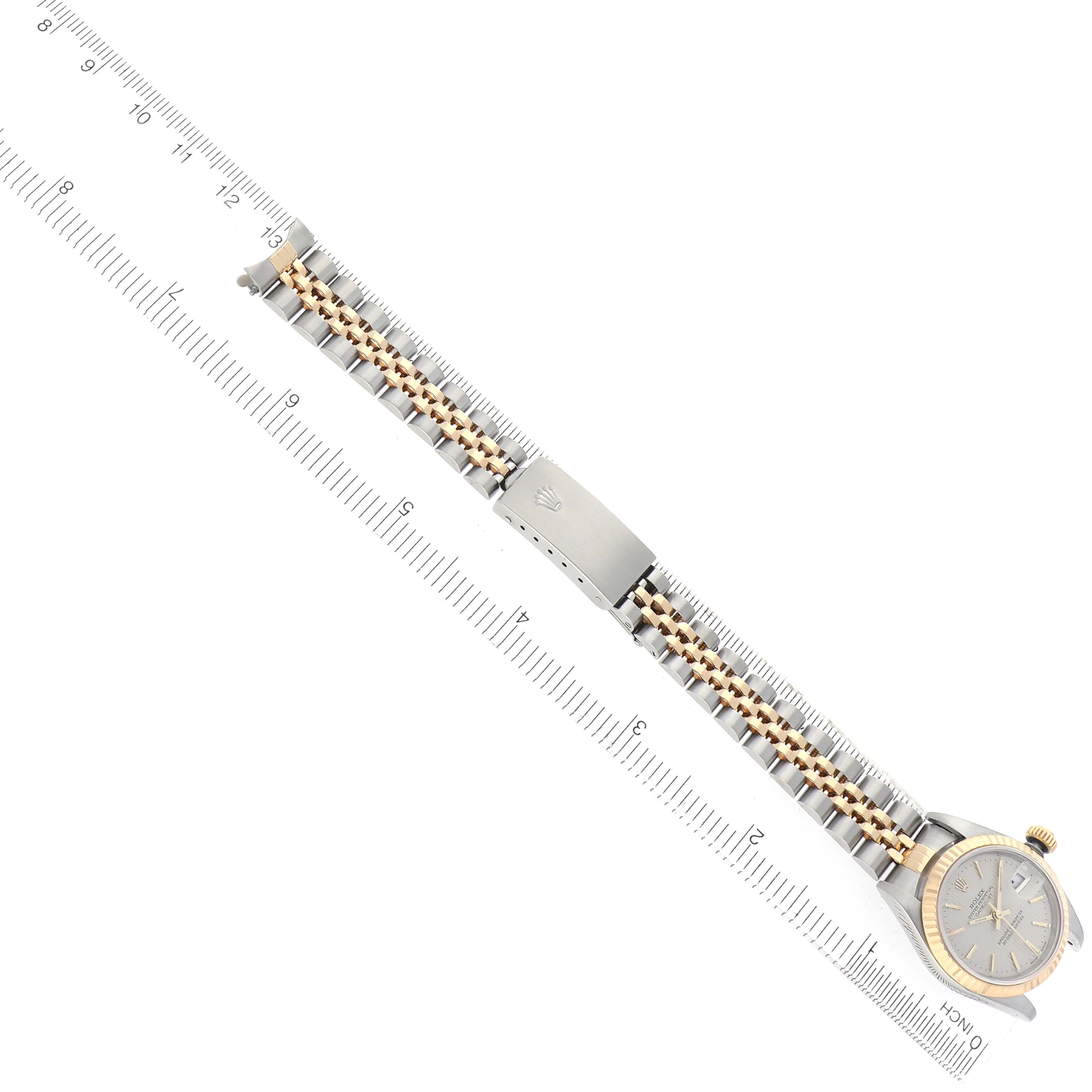 The Rolex Datejust 79173 Women's Steel and Gold (two tone) Silver Dial 79173 Women's Steel and Gold (two tone) Silver Dial watch is shown from above, with focus on its bracelet and clasp, alongside a ruler for scale.
