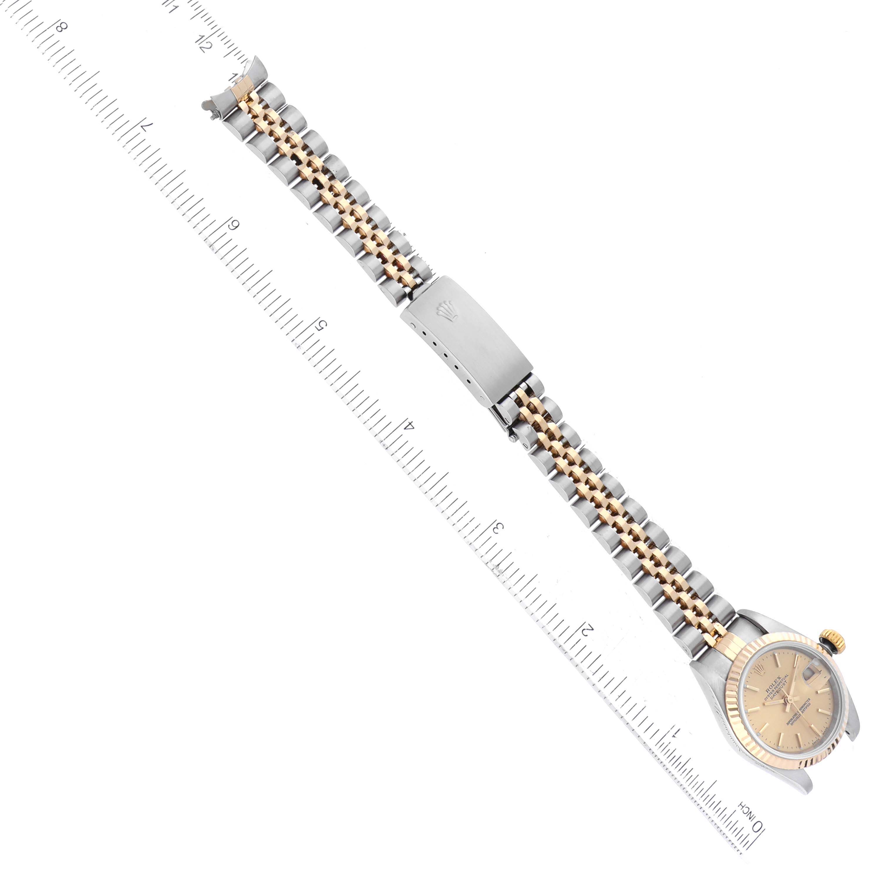 The image shows a top-down view of the Rolex Datejust 79173 Women's Steel and Gold (two tone) Champagne Dial 79173 Women's Steel and Gold (two tone) Champagne Dial watch, highlighting its bracelet, clasp, and face against a measurement ruler.