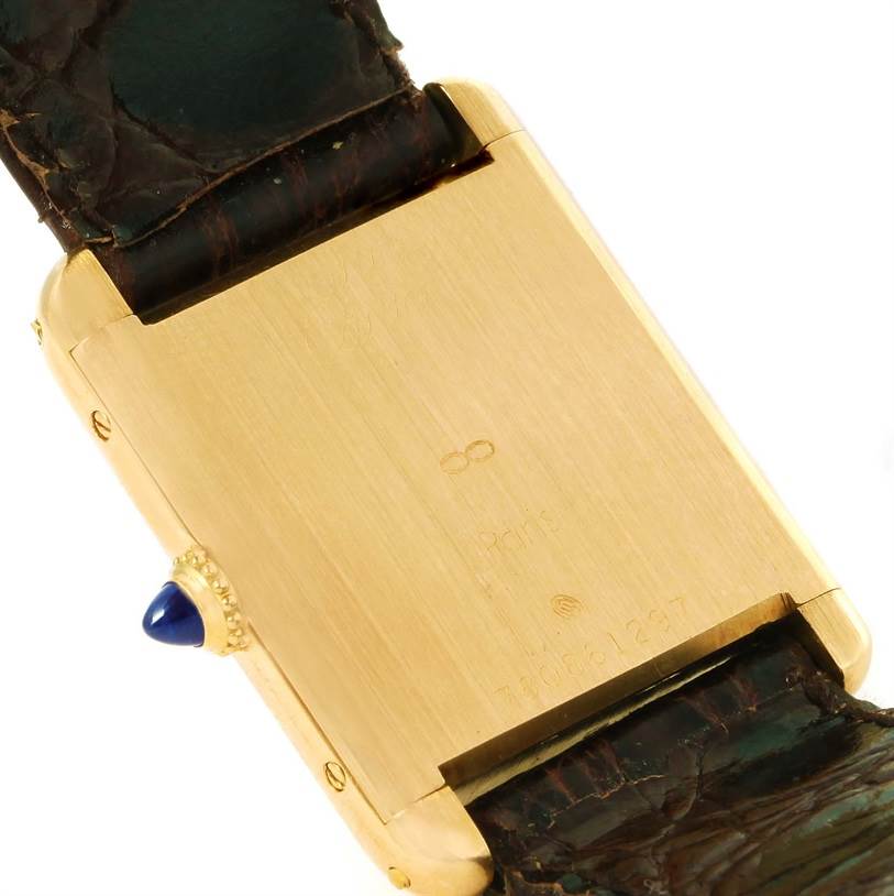 The image shows the back of a Cartier Tank Classic Men's Yellow Gold White Dial Men's Yellow Gold White Dial watch, highlighting its gold case and dark leather strap.