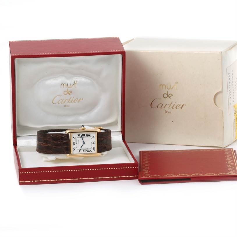 The Cartier Tank Classic Men's Yellow Gold White Dial Men's Yellow Gold White Dial watch is shown front-facing in its red box, along with its outer box and booklet.