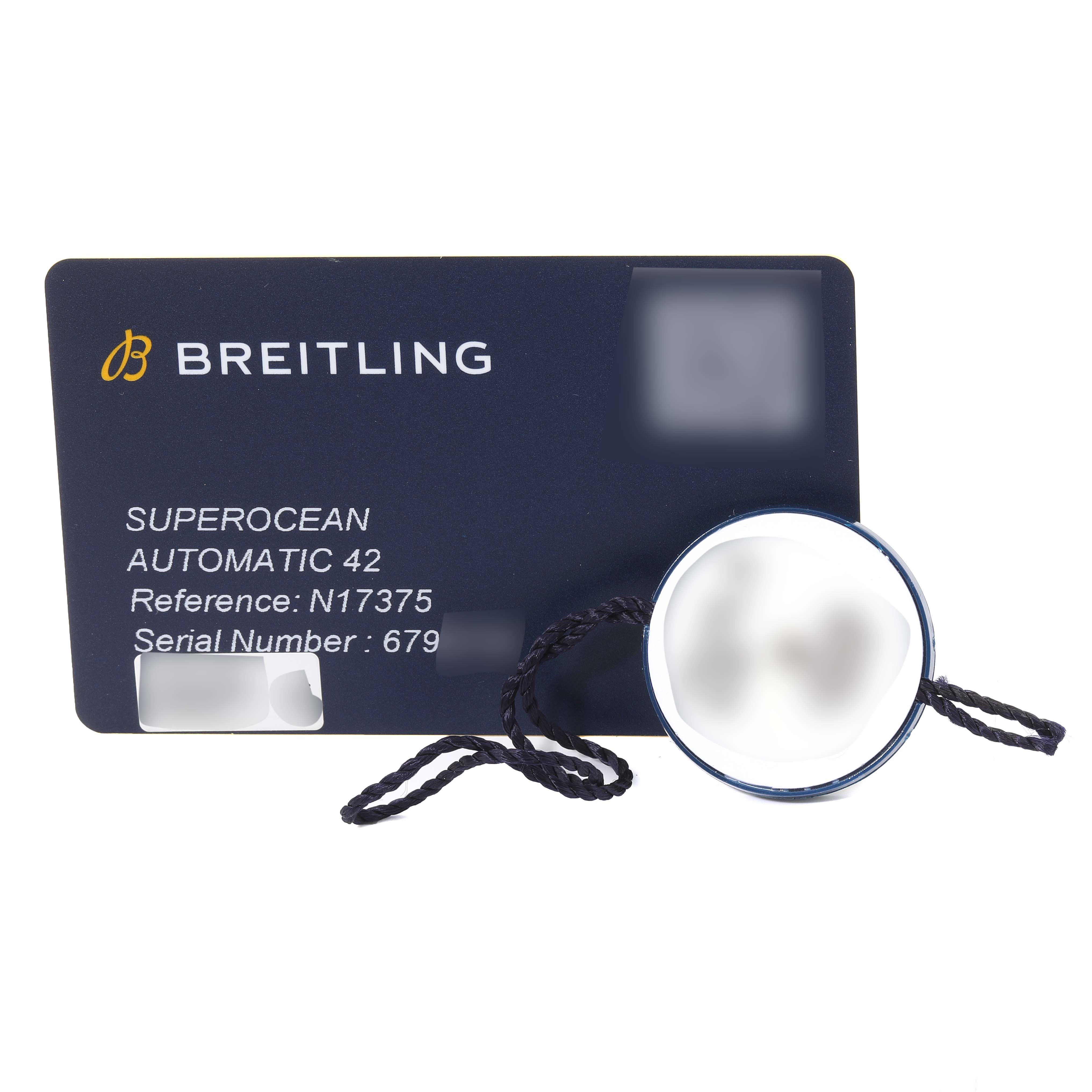 This image shows a Breitling Superocean N17375 Men's Yellow Gold Green Dial N17375 Men's Yellow Gold Green Dial model certification card and a round tag with string attached.