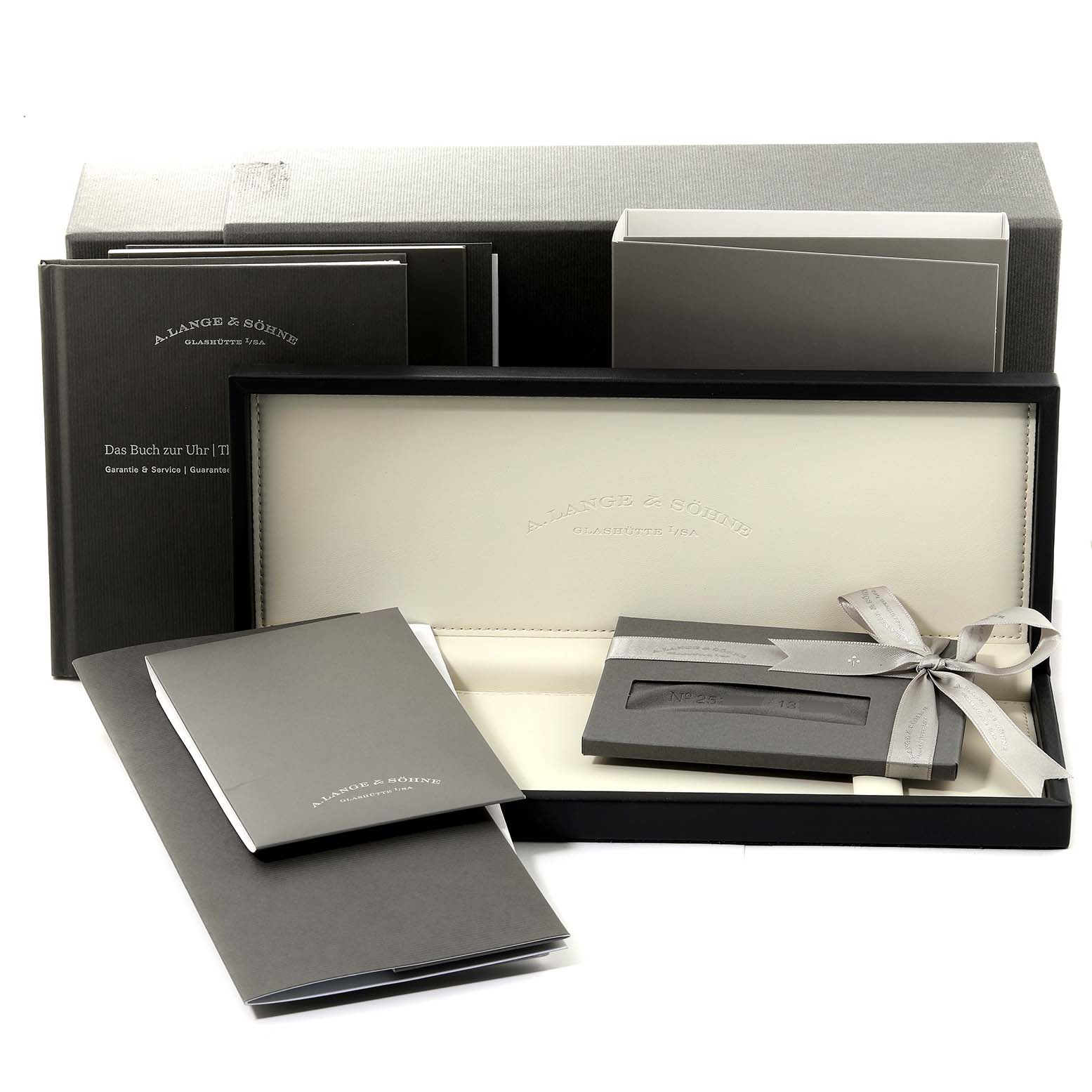 The image shows the packaging and accessories for the 1815 model by A. Lange & Söhne, including the watch box, manuals, and paperwork.