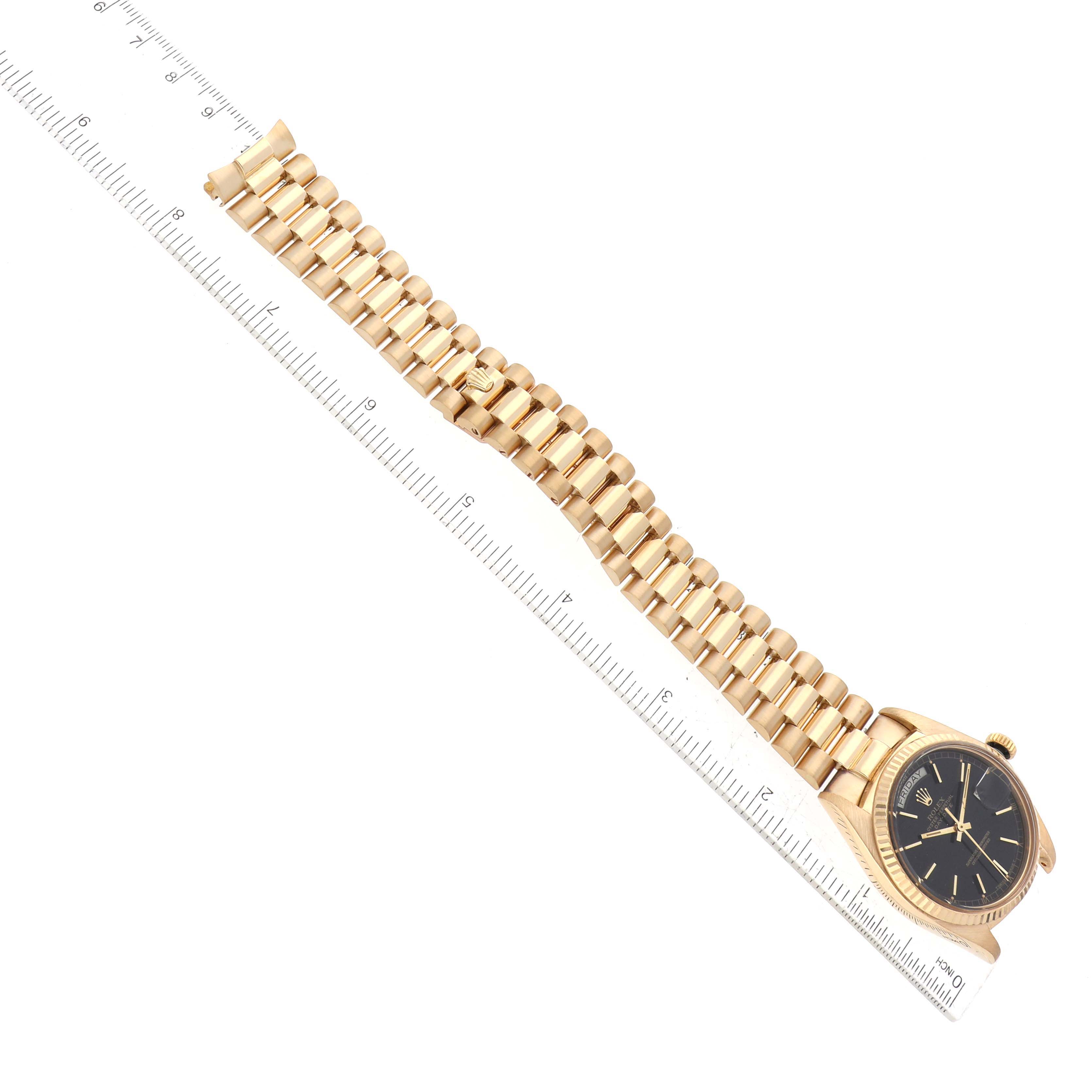 The image shows a full side angle of a Rolex President 18038 Men's Yellow Gold Black Dial 18038 Men's Yellow Gold Black Dial model watch with a gold bracelet next to a ruler.