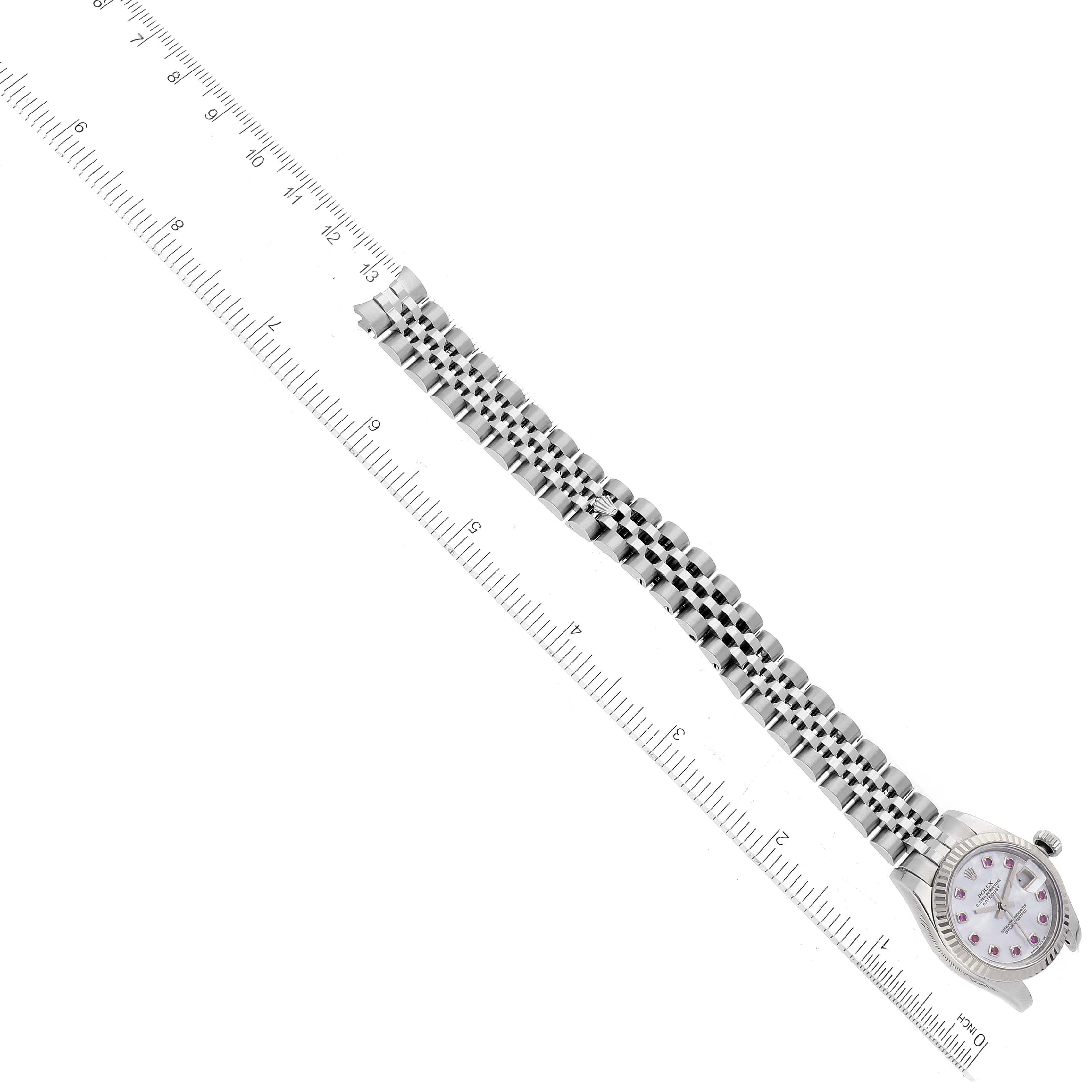 This image shows a Rolex Datejust 179174 Women's Stainless Steel Mother of Pearl Dial 179174 Women's Stainless Steel Mother of Pearl Dial watch laying flat, with its face at the bottom left and the metal bracelet aligned along a ruler.
