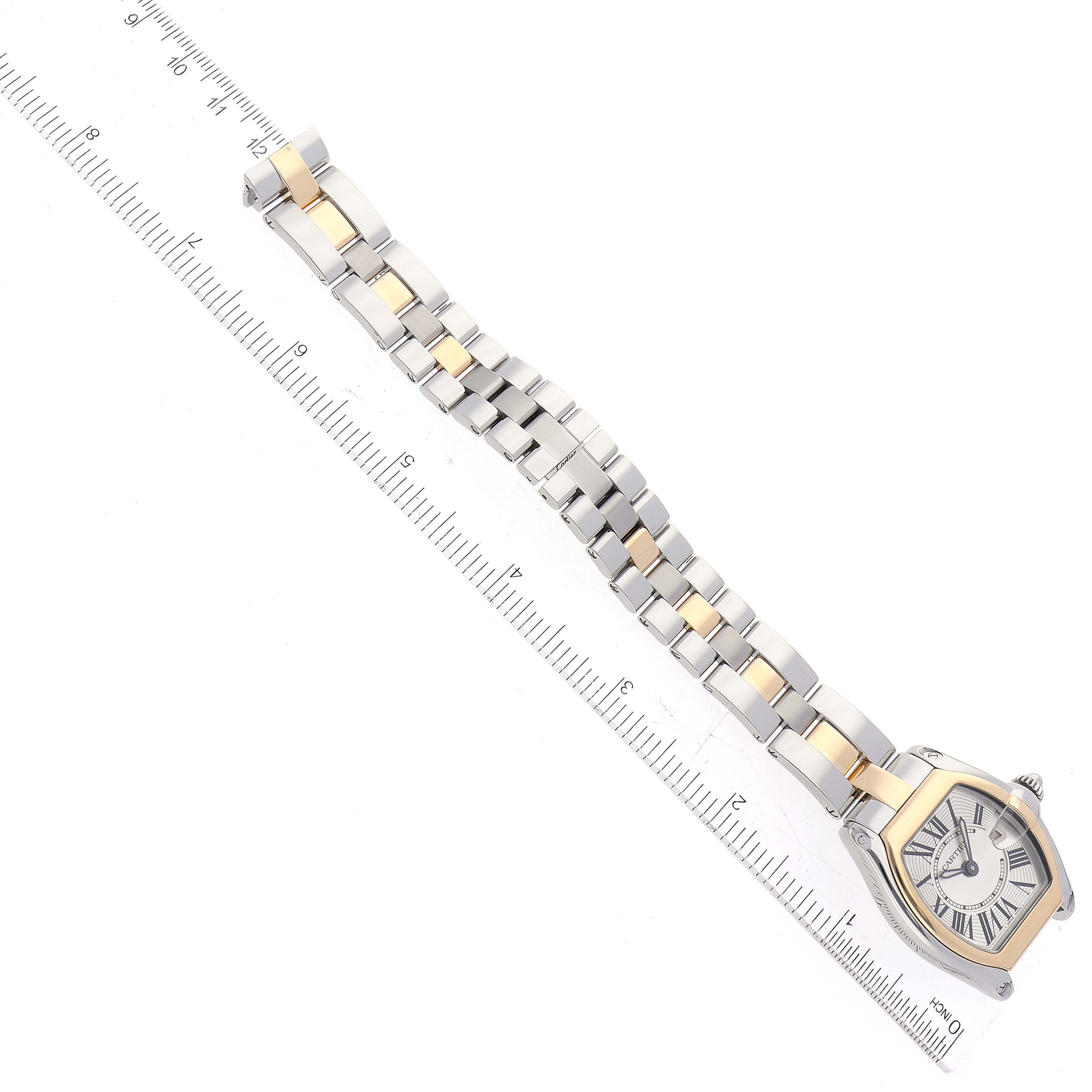 The Cartier Roadster W62026Y4 Women's Steel and Gold (two tone) Silver Dial W62026Y4 Women's Steel and Gold (two tone) Silver Dial watch is shown from a top-down angle, displaying the face, bezel, and full bracelet alongside a ruler.