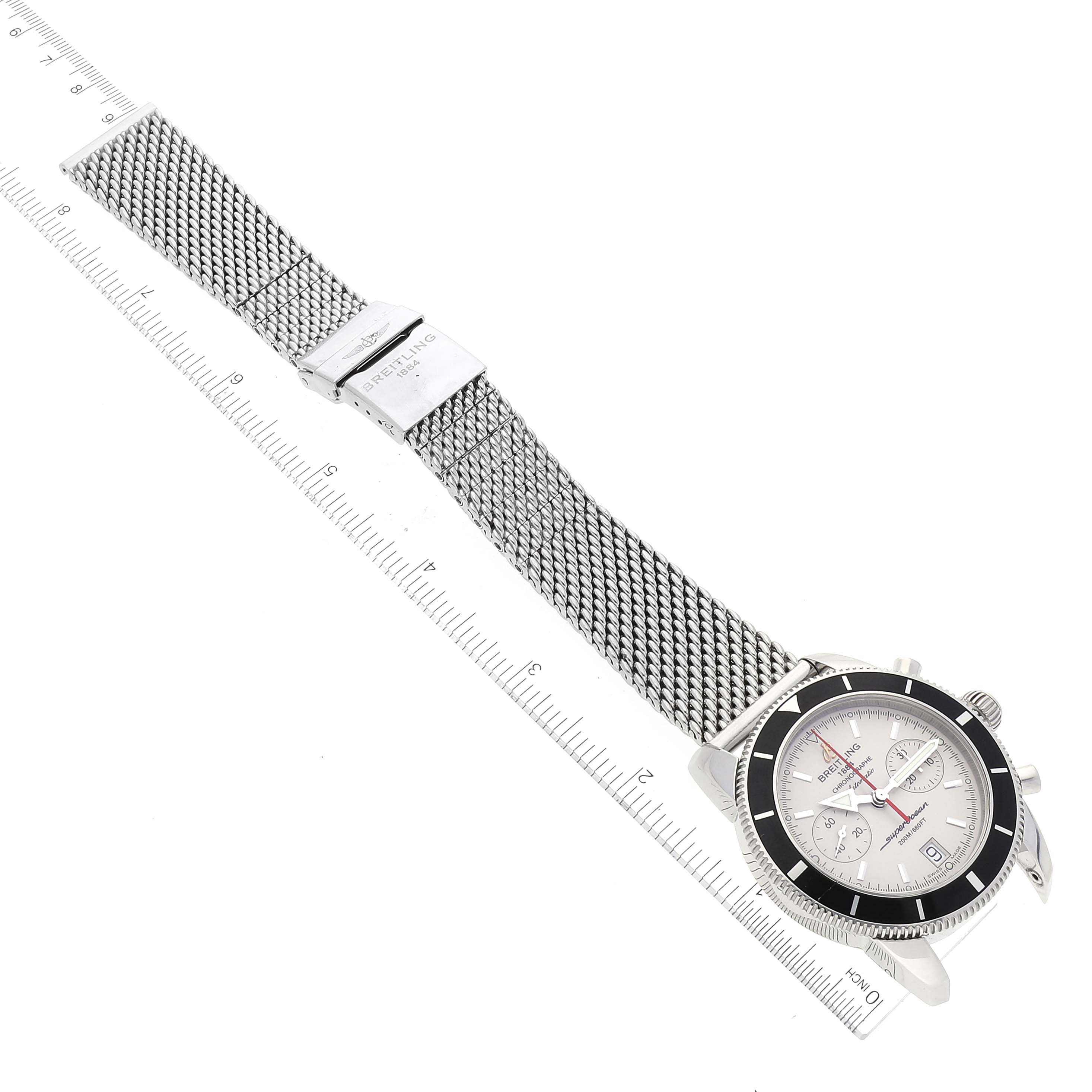The image shows a top-down view of a Breitling Superocean A23370 Men's Stainless Steel Silver Dial A23370 Men's Stainless Steel Silver Dial watch with a mesh bracelet next to a ruler for scale.